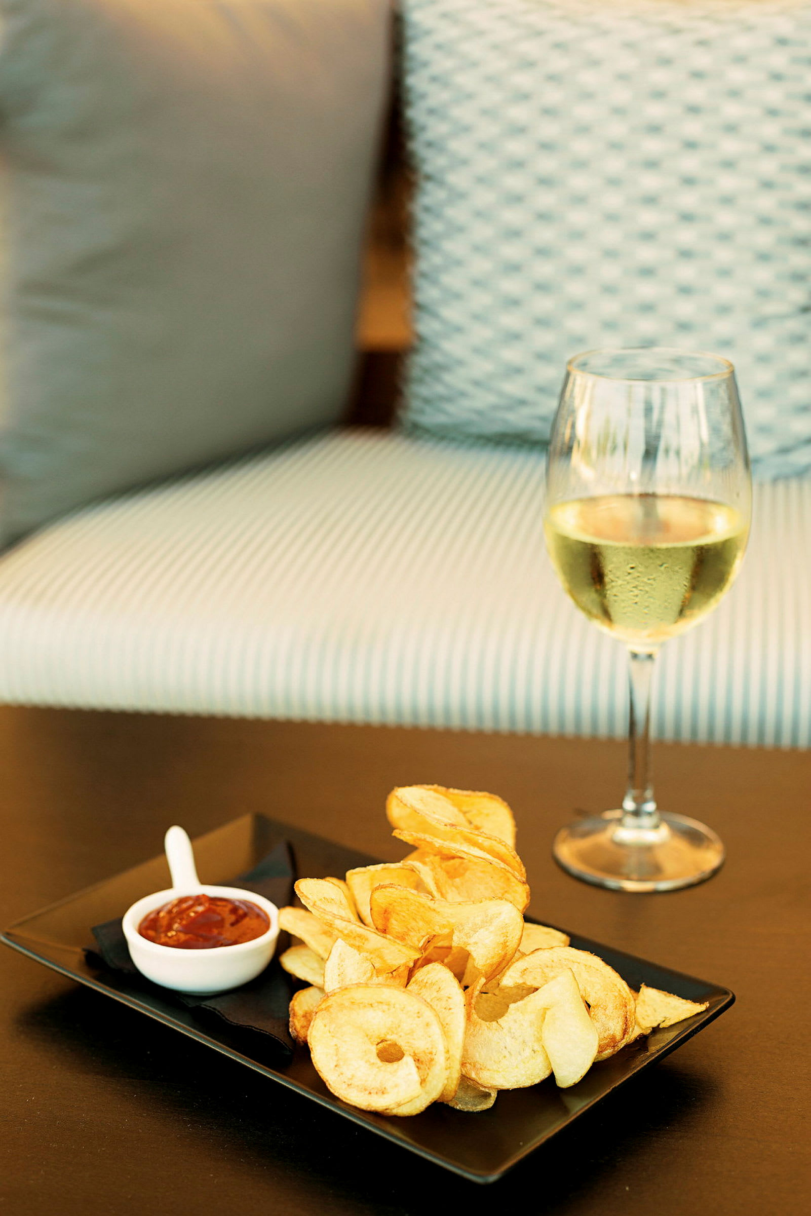 Et glas hvidvin ved siden af en tallerken med chips og dip. (AI-genereret tekst)