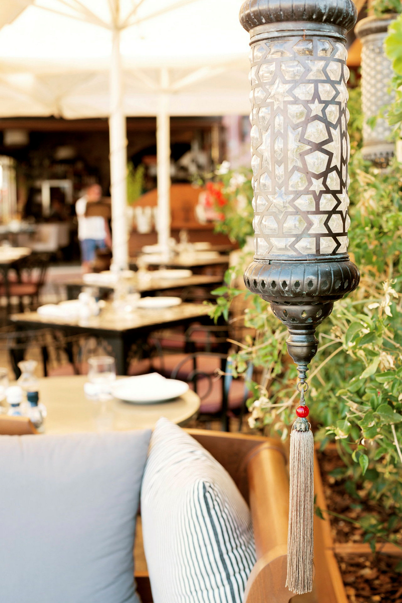 Nærbillede af en dekorativ lampe med geometrisk mønster og frynser, med en restaurantbaggrund. (AI-genereret tekst)