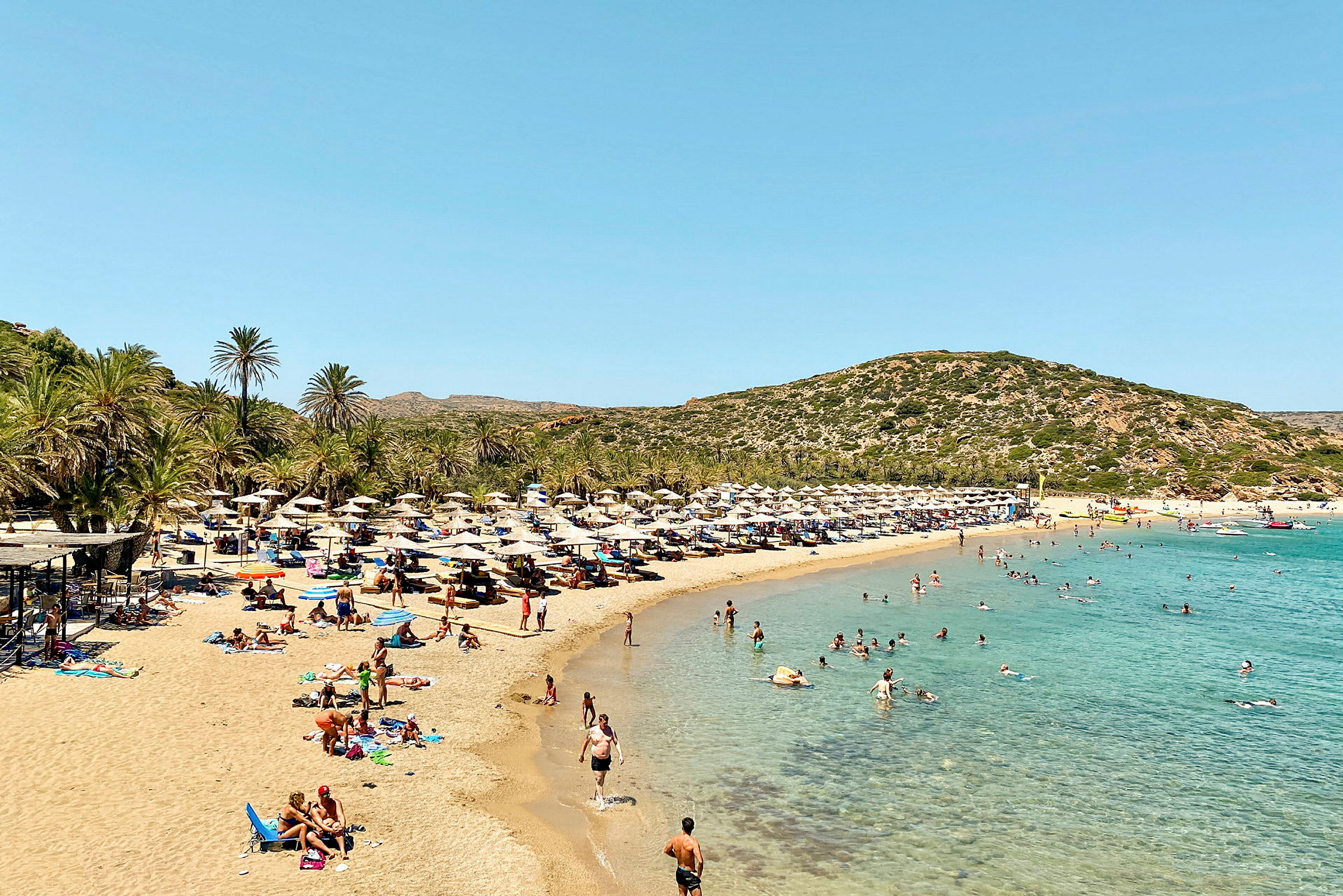 En sandstrand med turkis vand, flankeret af liggestole og parasoller under palmer. (AI-genereret tekst)