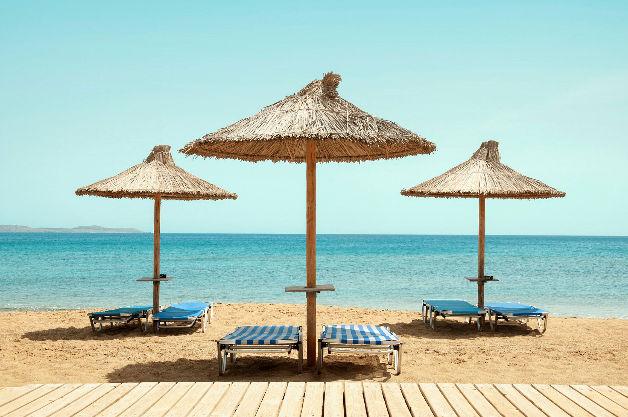 Tre parasoller med liggestole på en sandstrand ved havet. (AI-genereret tekst)
