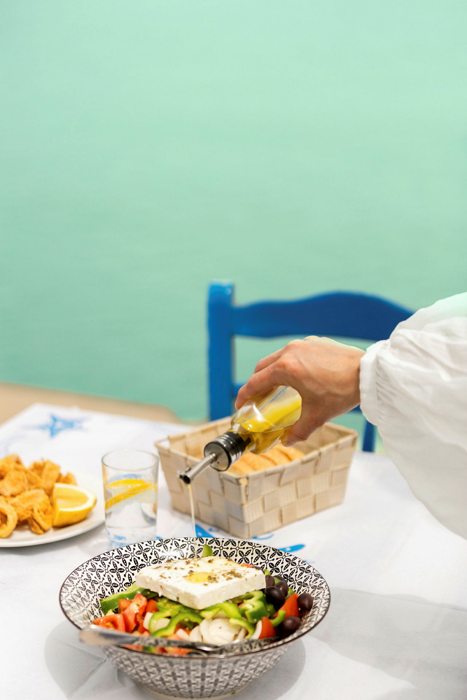 En hånd hælder olivenolie over en græsk salat på et bord. (AI-genereret tekst)