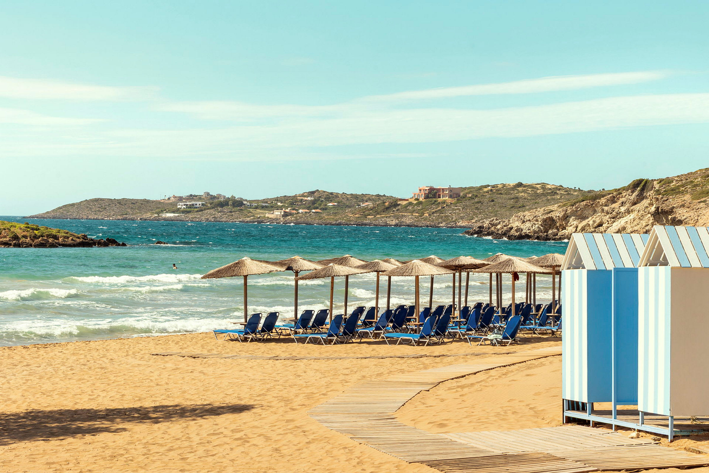 Strand med parasoller og liggestole, en strandpromenade i træ og små farverige strandhytter. (AI-genereret tekst)