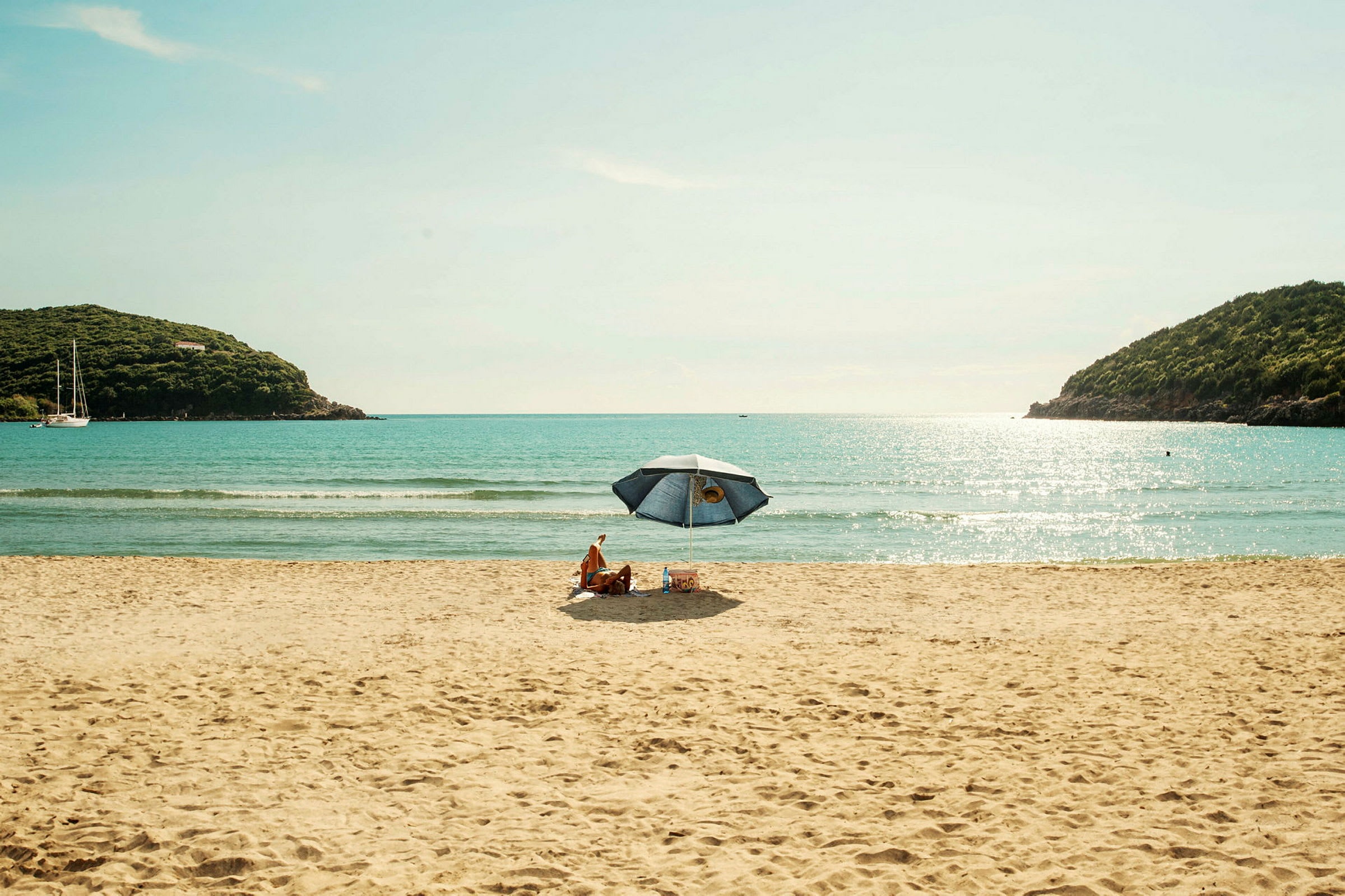 Personer sidder under en parasol på en sandstrand med havet i baggrunden. (AI-genereret tekst)