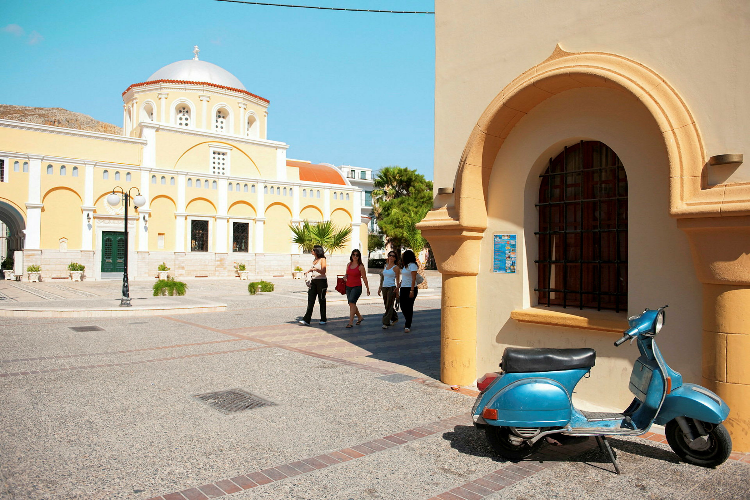 Gul kirkelig bygning med kuppelformet tag, arkitektoniske detaljer og en blå scooter i forgrunden. (AI-genereret tekst)