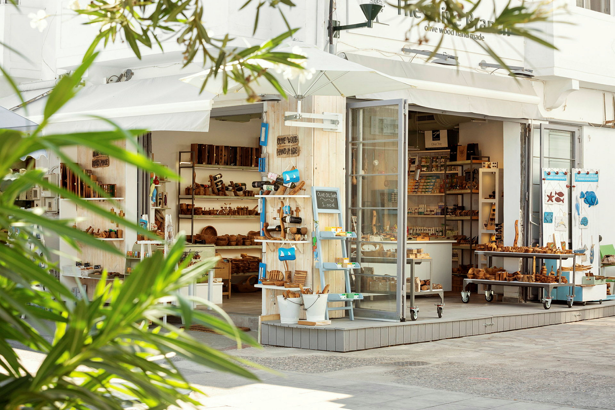 En butik med træprodukter og souvenirs, med en åben glasfacade og grønt i forgrunden. (AI-genereret tekst)