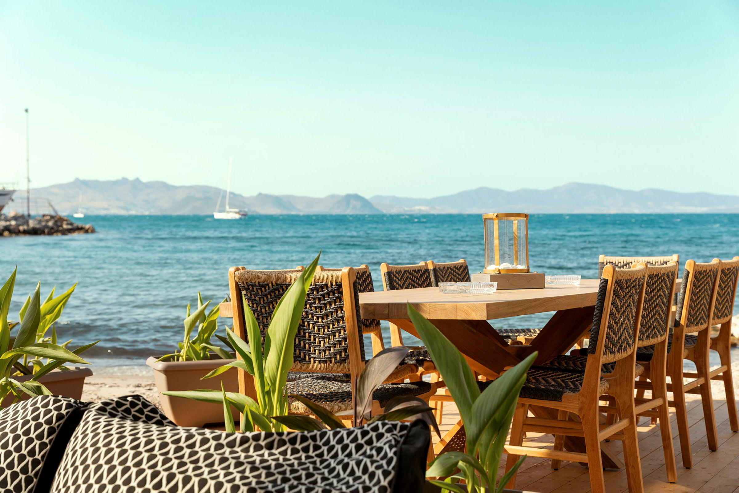 Træbord med stole på en terrasse tæt på havet. (AI-genereret tekst)