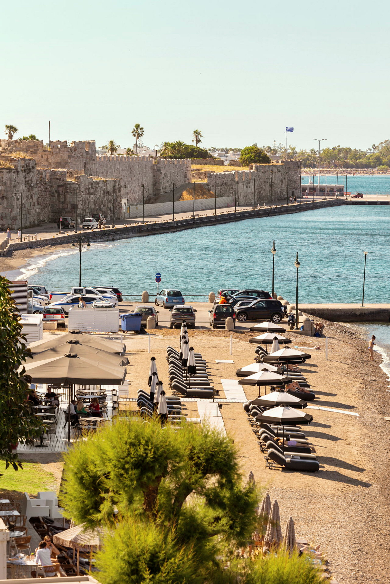 Strand med solvogne og parasoller nær klippevægge og blåt hav. (AI-genereret tekst)