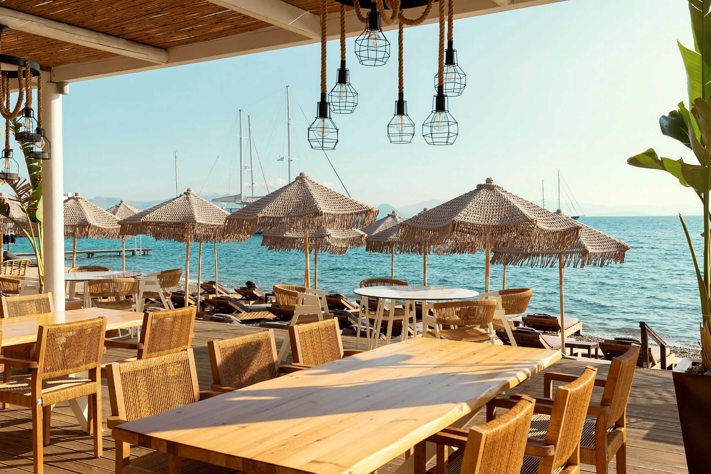 Strandrestaurant med borde og stole, parasoller og udsigt over havet. (AI-genereret tekst)