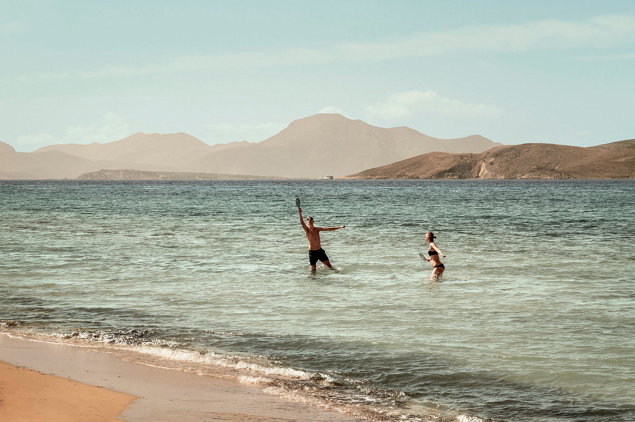 To personer spiller strandtennis i vandet ved en strand. (AI-genereret tekst)