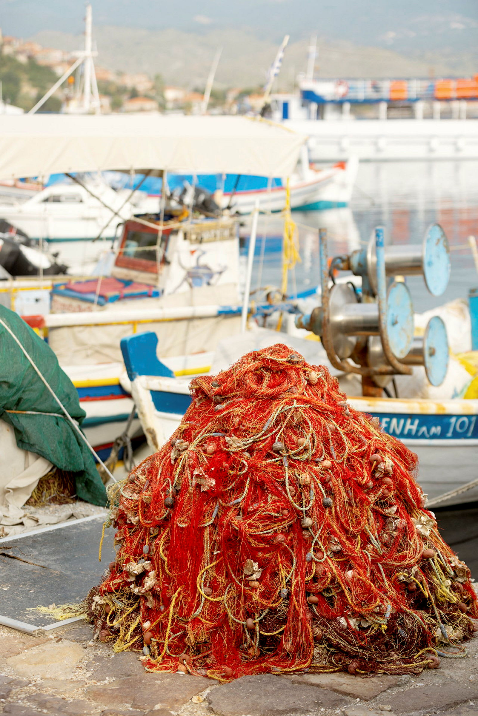En bunke af røde og gule fiskegarn ligger på kajen nær fortøjede både. (AI-genereret tekst)