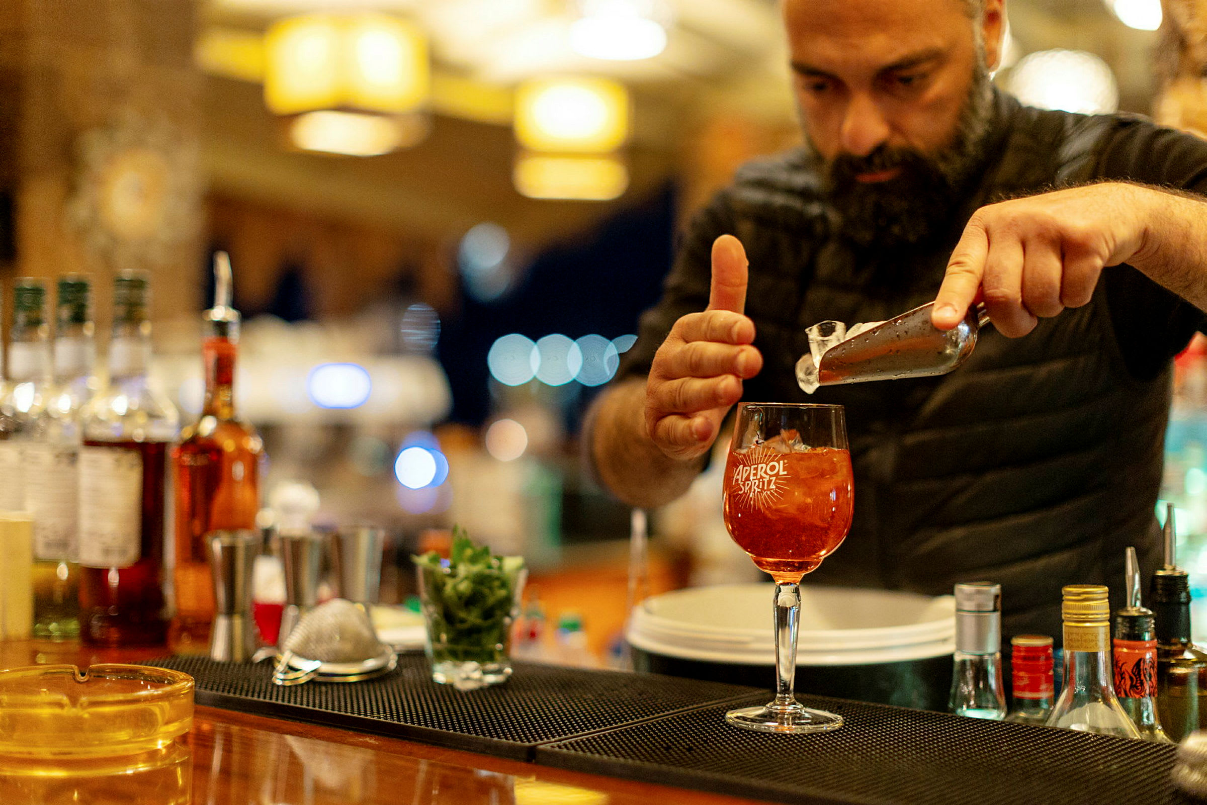 En person forbereder en Aperol Spritz ved en bardisk. (AI-genereret tekst)