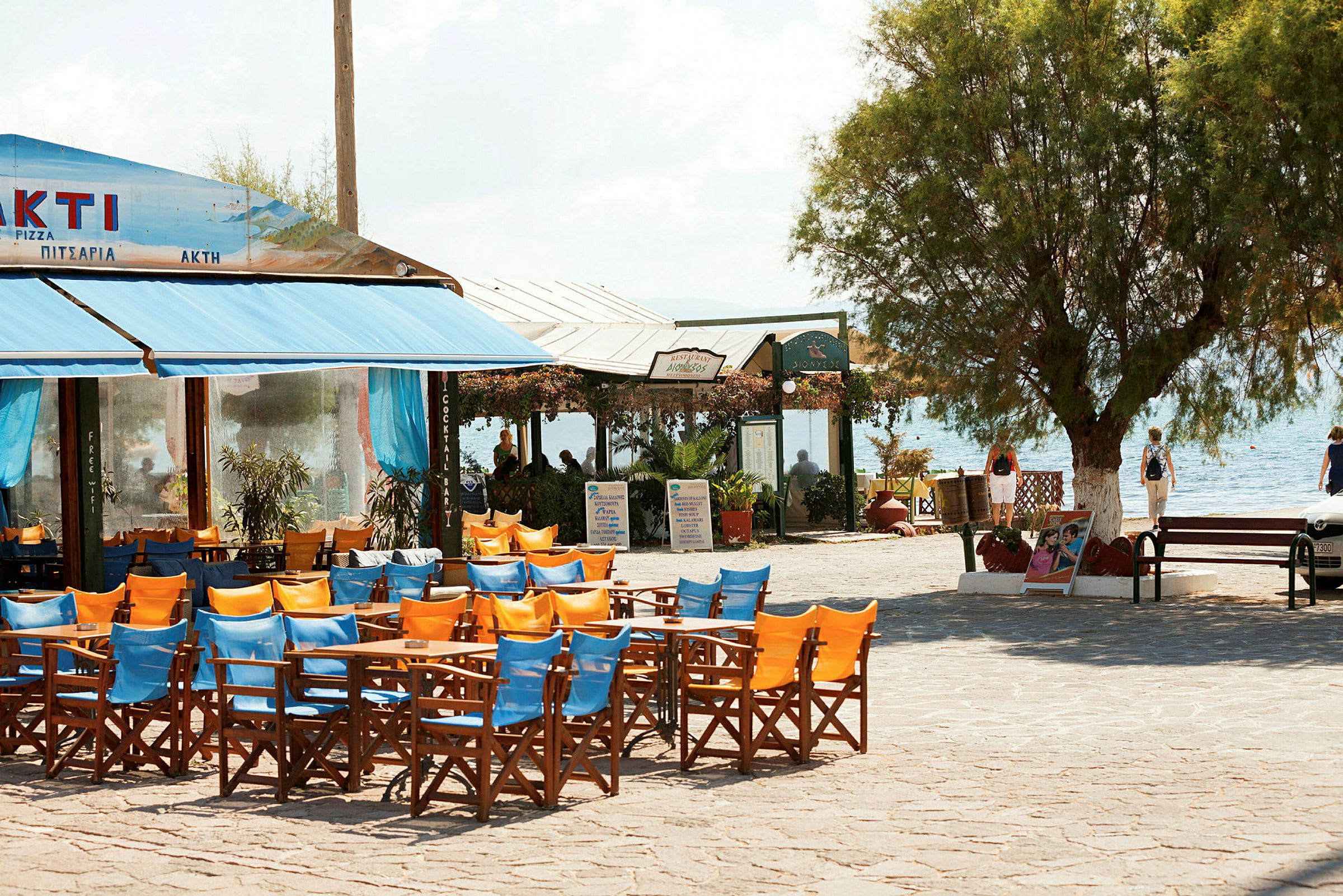 En udendørsrestaurant med farverige stole og borde med havet i baggrunden. (AI-genereret tekst)