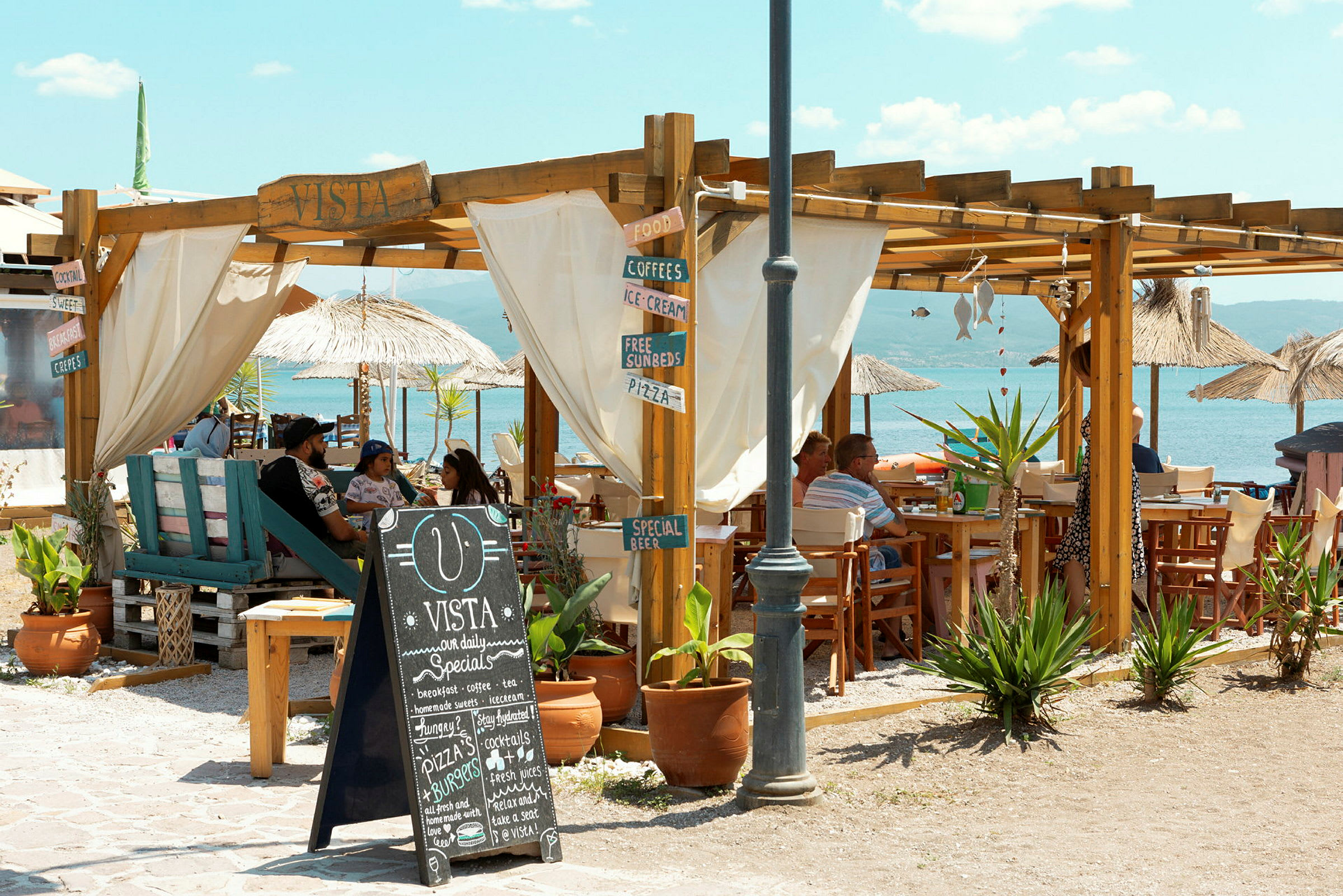 Udendørsområde på en strandcafé med trækonstruktioner og borde, tæt på havet. (AI-genereret tekst)