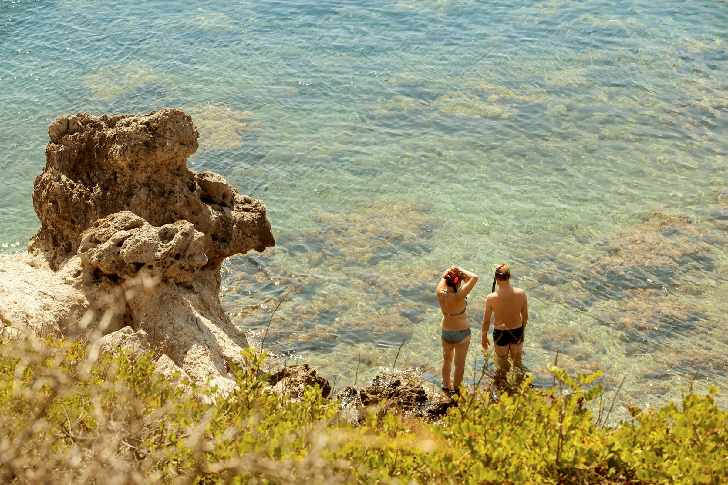 To personer står i klart vand ved en klippe, udstyret med snorkeludstyr. (AI-genereret tekst)