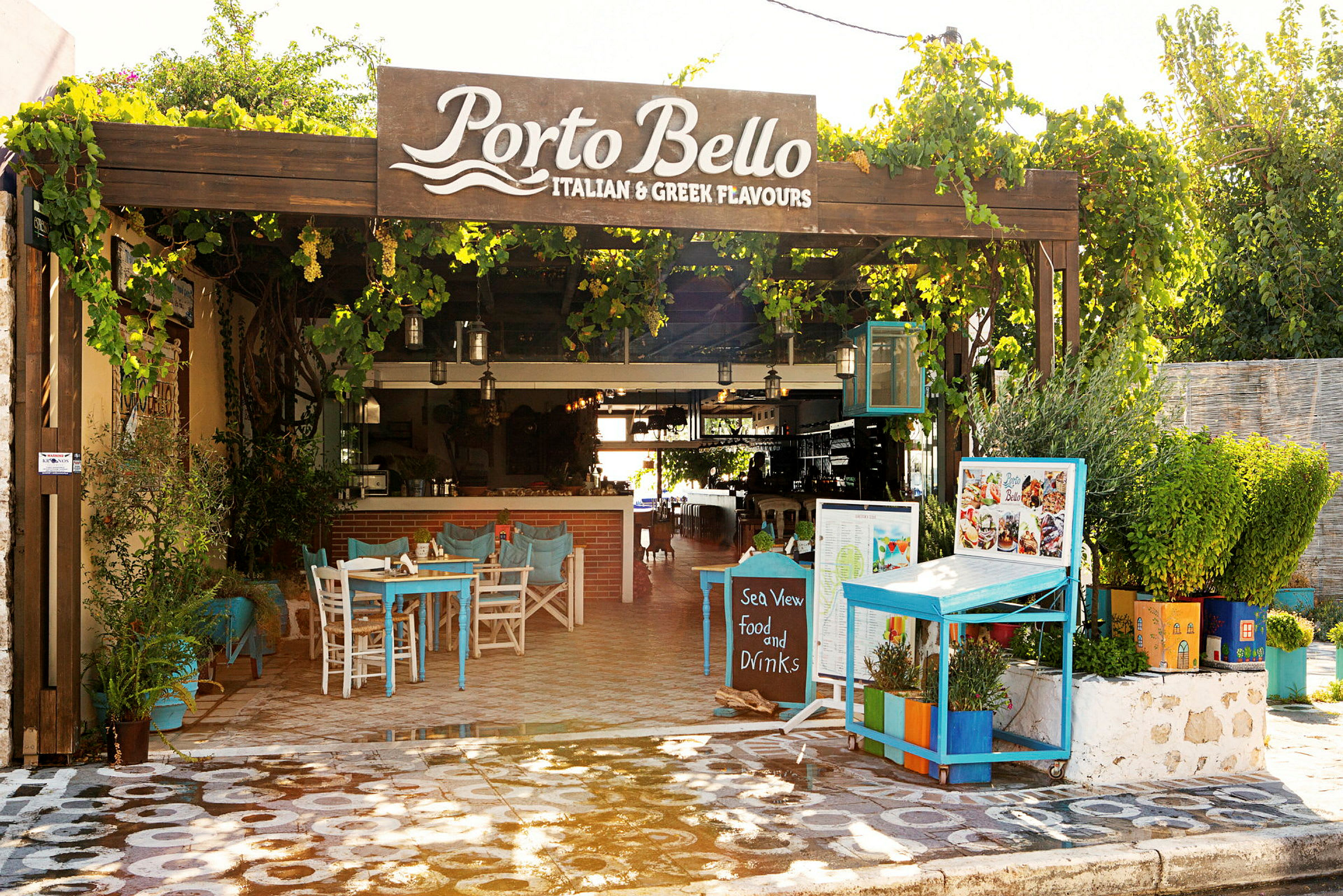Billede af en udendørsrestaurant kaldet Porto Bello med borde og planter. (AI-genereret tekst)