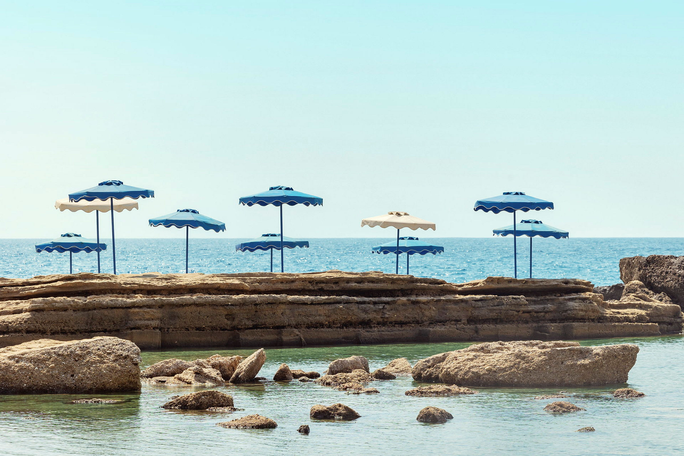 Strand med parasoller og klipper ved havet. (AI-genereret tekst)