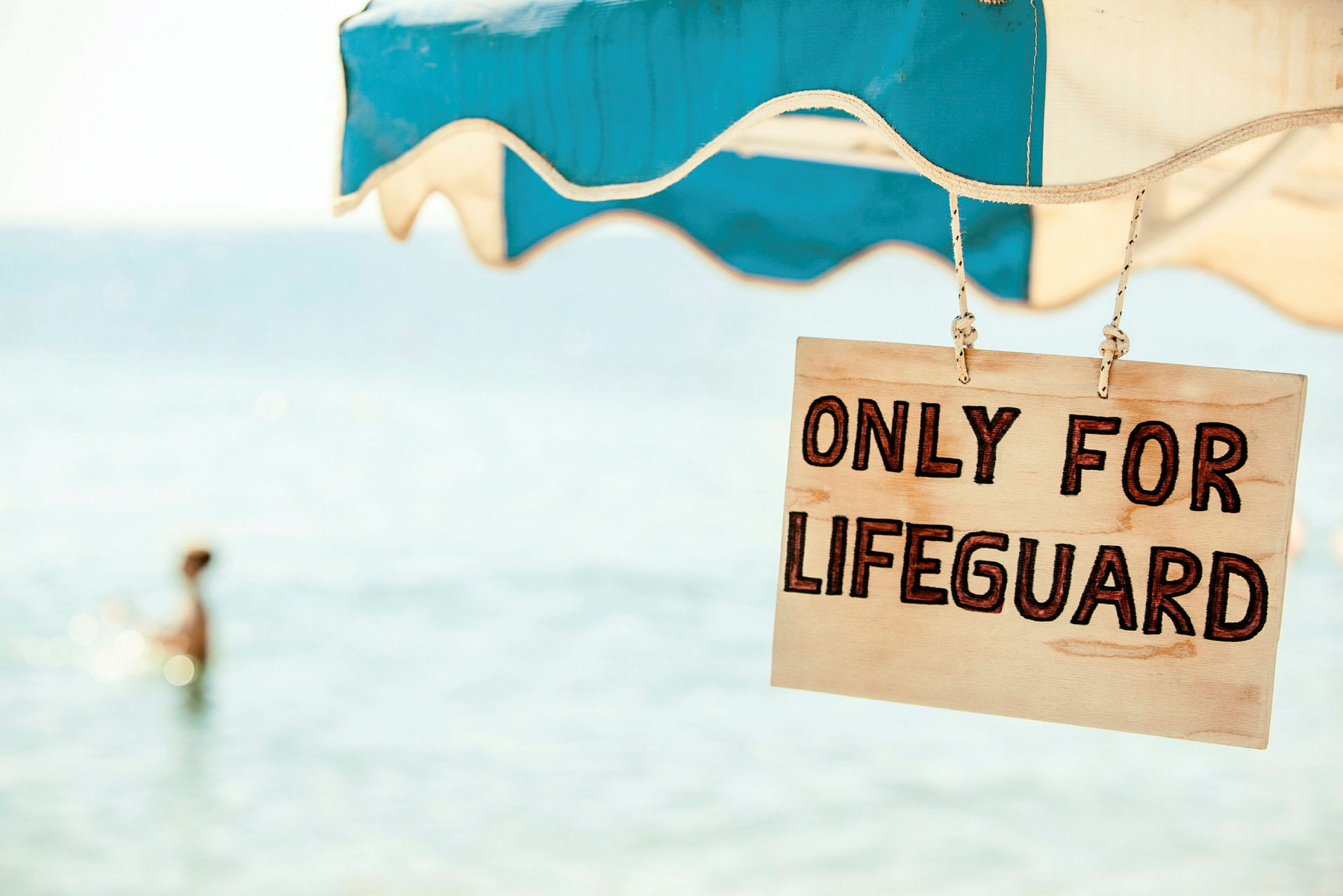 Skilt med teksten 'Only for lifeguard' hængt op under en parasol nær havet. (AI-genereret tekst)