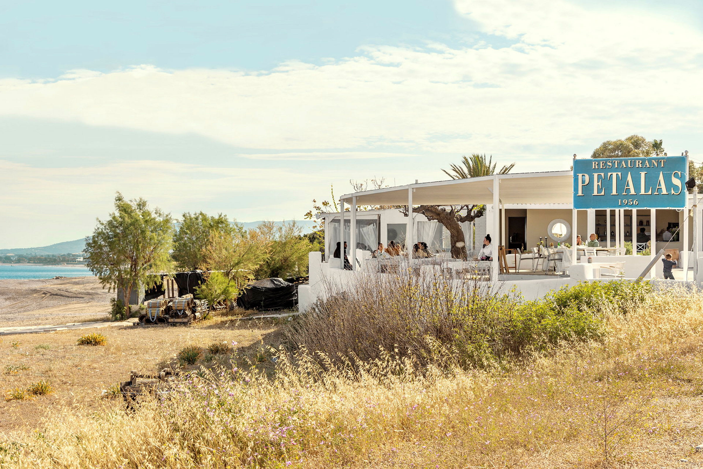 En restaurant med hvid bygning nær en strand med udendørs servering under tag. (AI-genereret tekst)