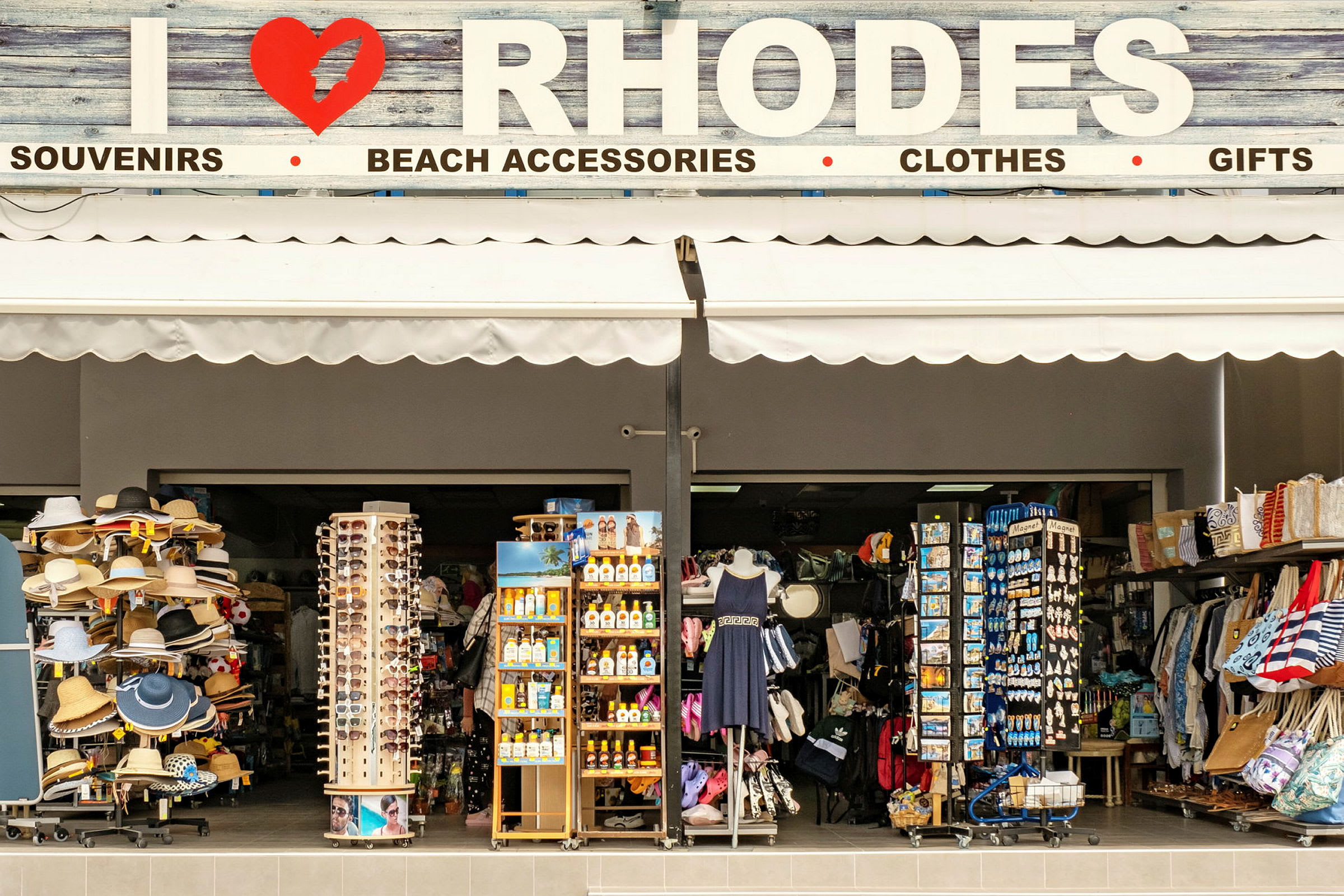 En butik, der sælger souvenirs og strandtilbehør med skiltet ovenover, der siger "I ❤ RHODOS". (AI-genereret tekst)