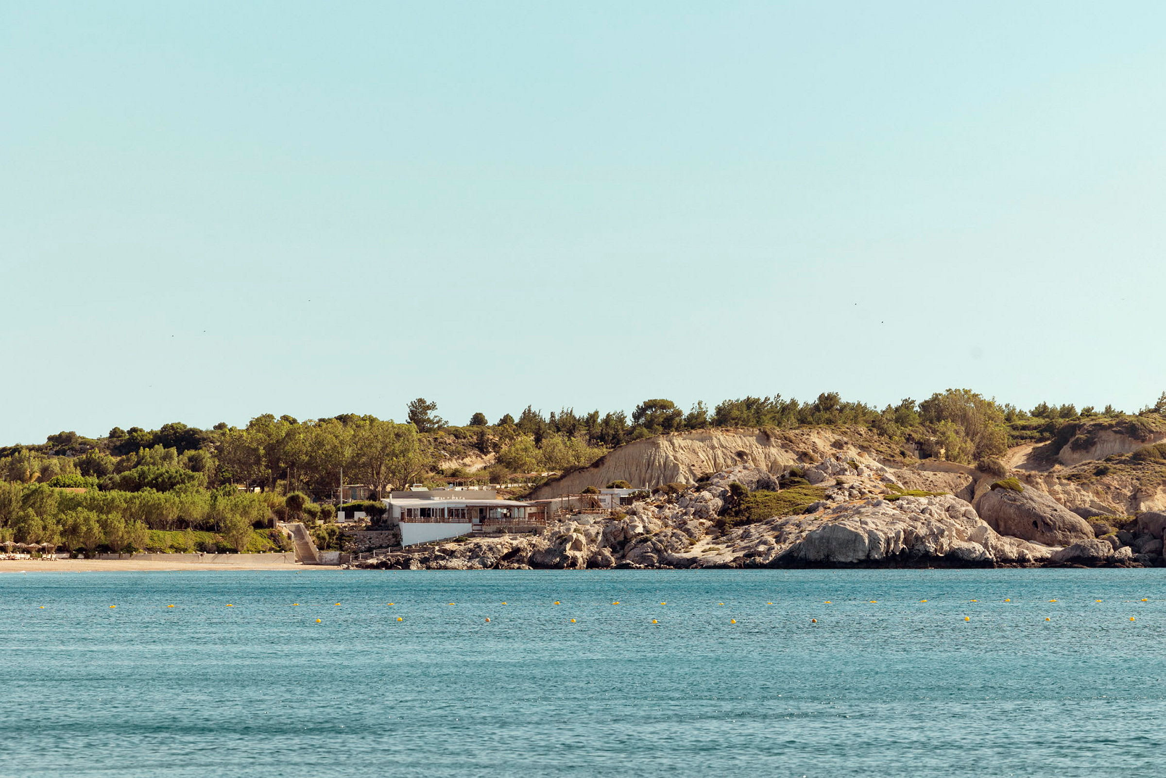 En strand og et hav med en bygning ved en klippefyldt kyst. (AI-genereret tekst)