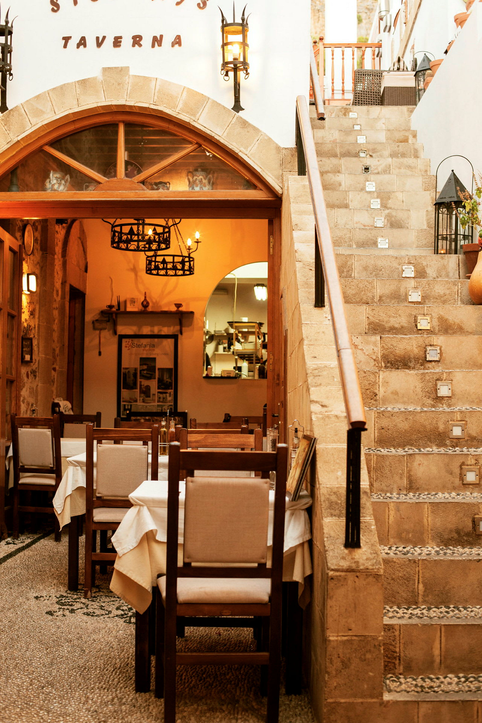 En taverna-interiør med borde og stole, samt en stenlagt trappe ved siden af. (AI-genereret tekst)