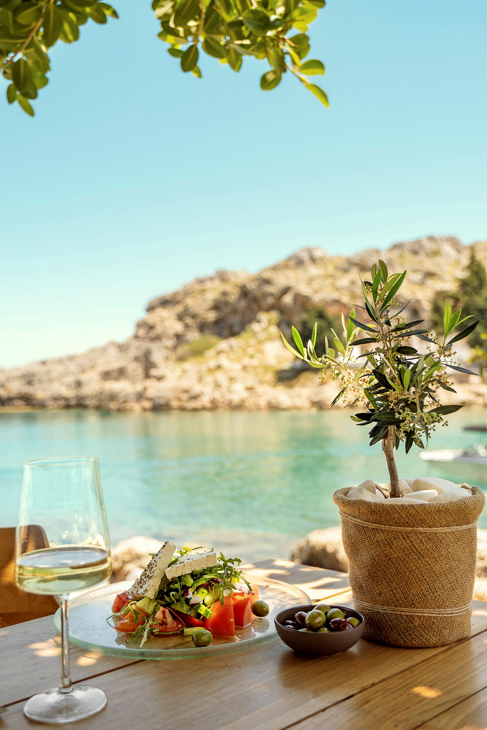 En frokost med græsk salat, et glas vin og oliven ved havet. (AI-genereret tekst)