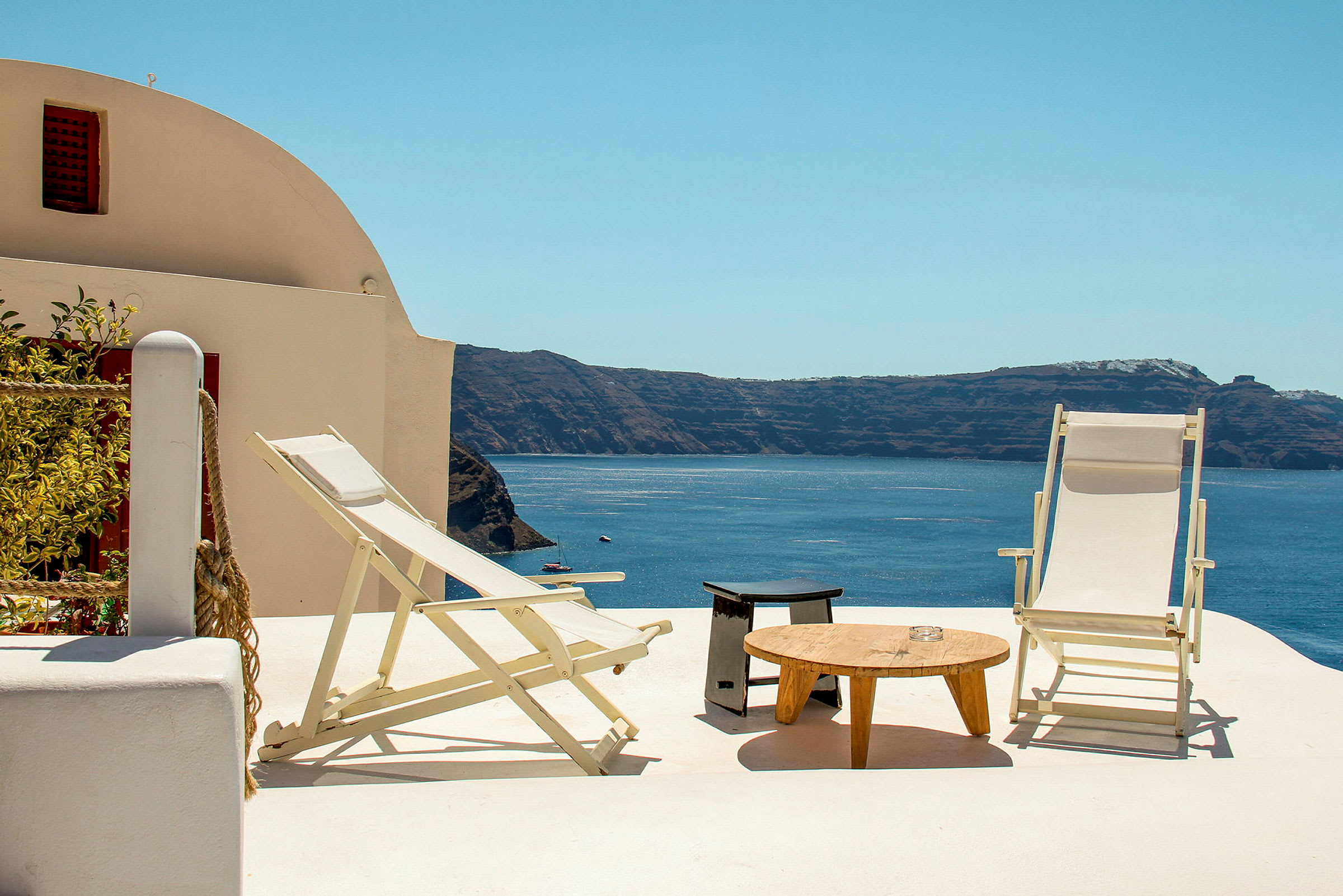 To liggestole og et bord på en terrasse med udsigt over havet og klipper. (AI-genereret tekst)