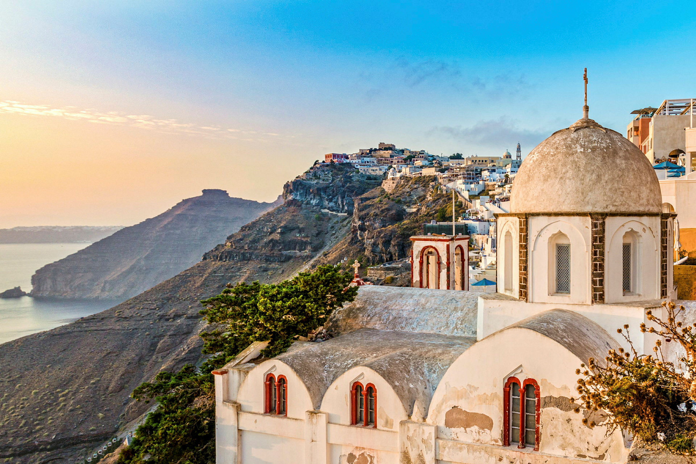 Udsigt over Santorini med sine karakteristiske hvide bygninger og en klippe ved havet i solnedgangen. (AI-genereret tekst)