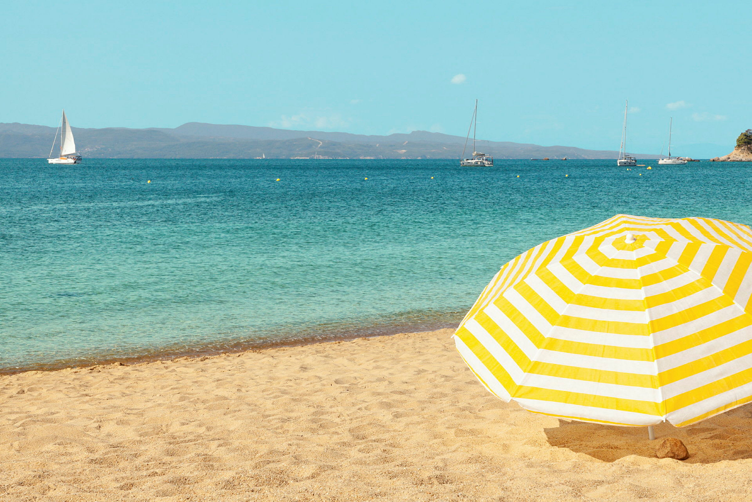 Gulstribet parasol på en sandstrand med havet i baggrunden. (AI-genereret tekst)