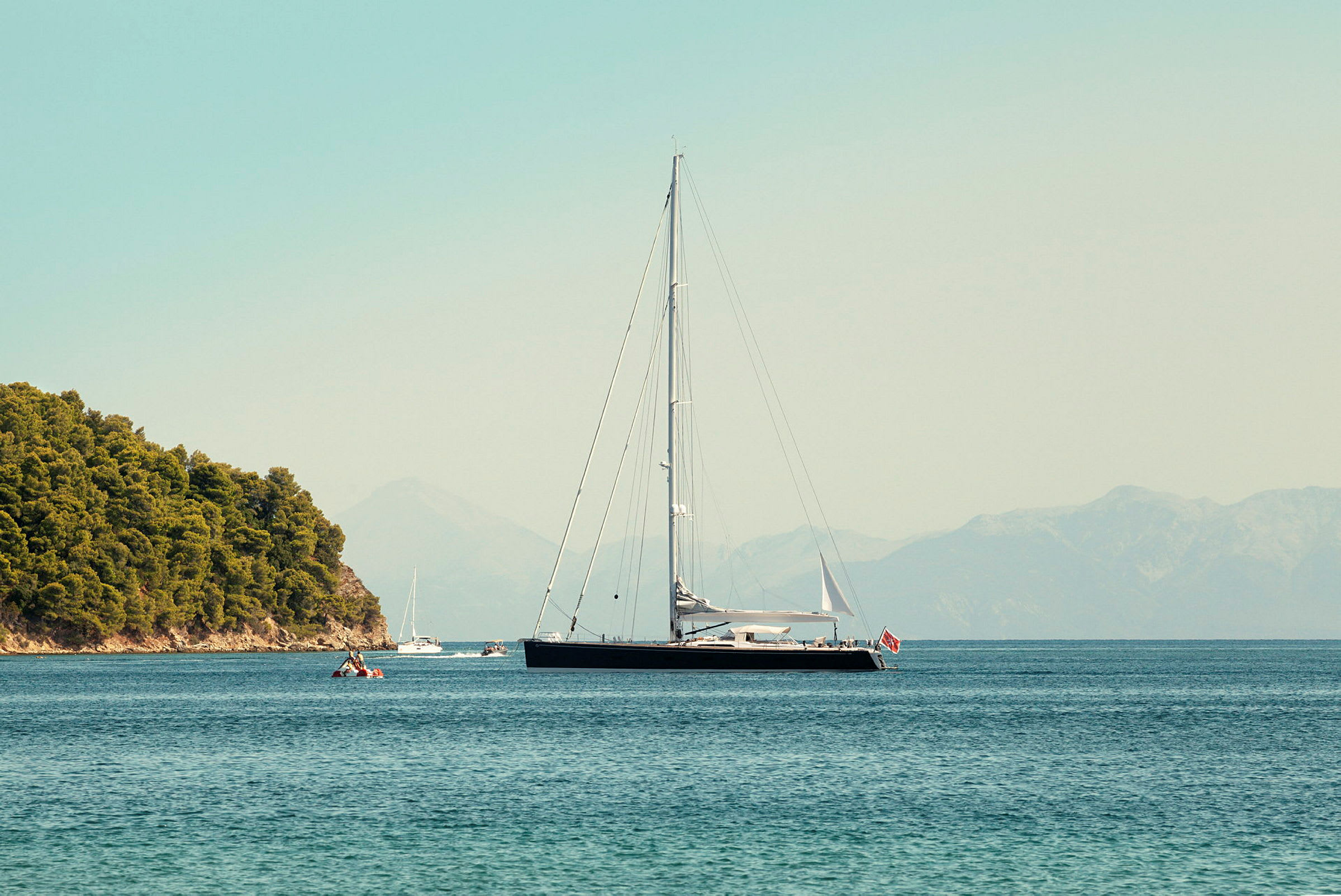 En sejlbåd ligger for anker nær en skovklædt kyst. (AI-genereret tekst)