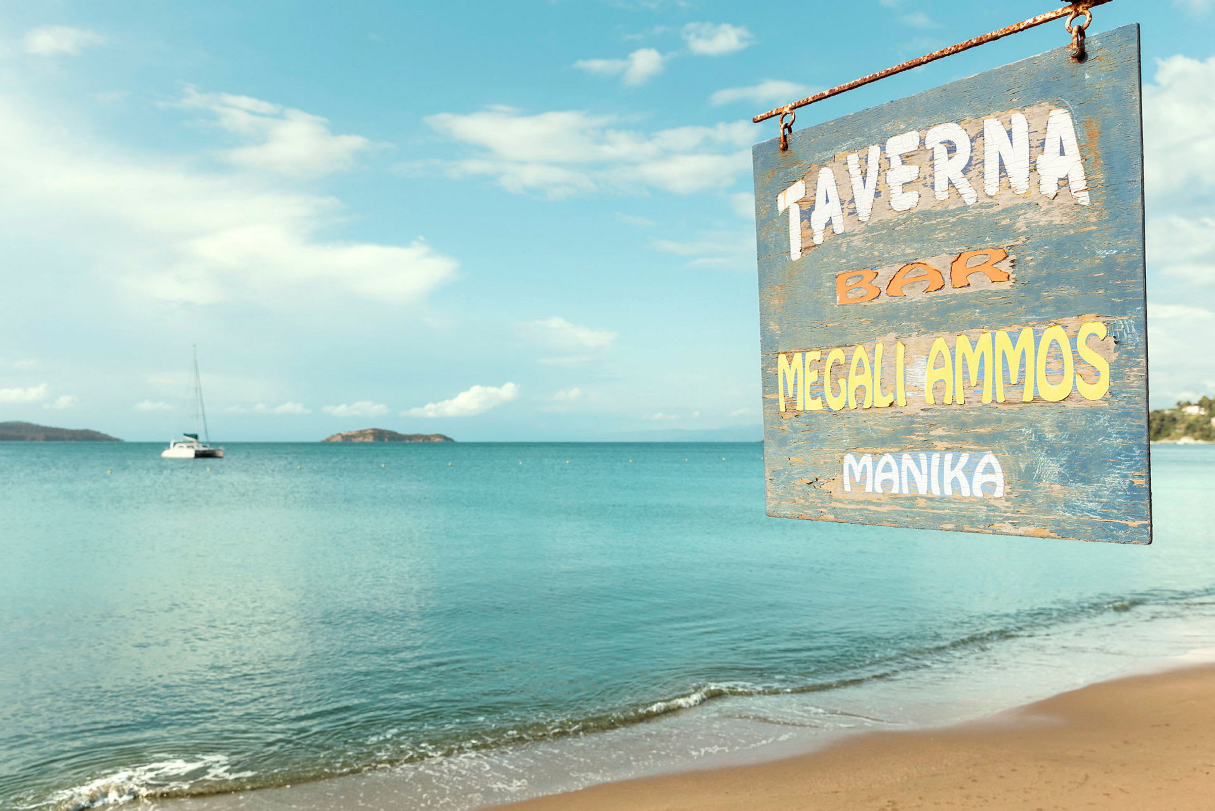 Skilt for en taverna ved en sandstrand med roligt hav i baggrunden. (AI-genereret tekst)