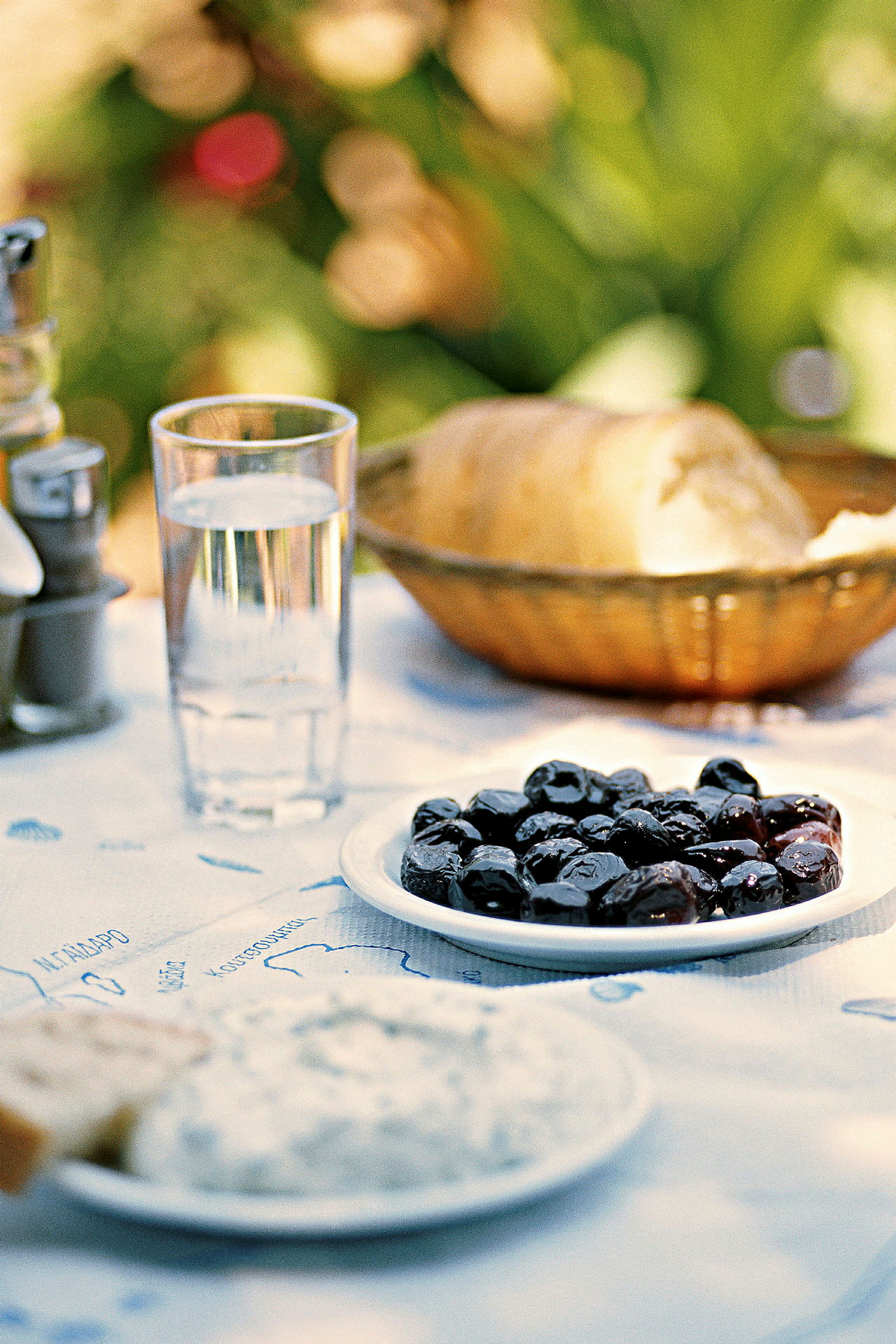 En tallerken med sorte oliven, et glas vand og et brød på et bord. (AI-genereret tekst)