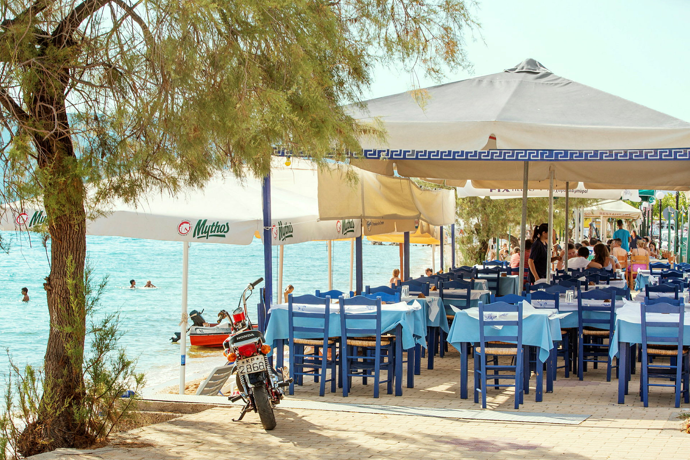 Restaurant med blå og hvide stole ved havet. (AI-genereret tekst)
