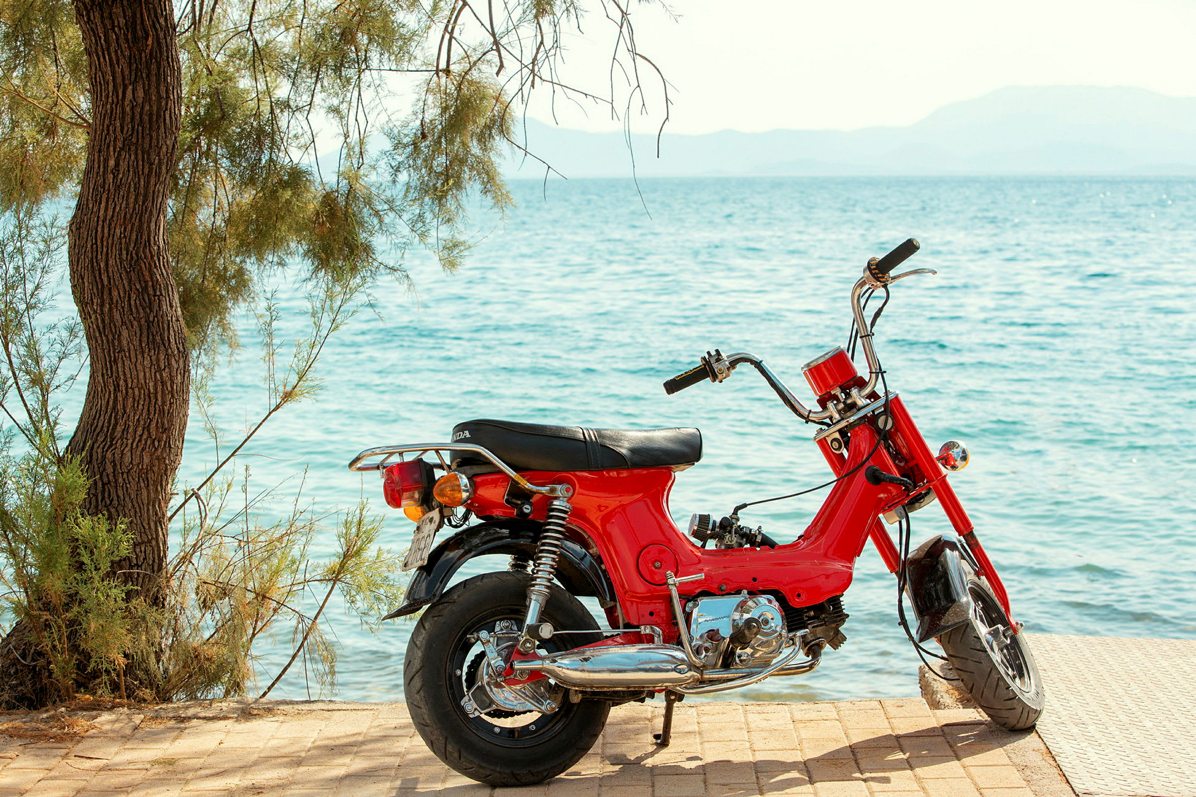 En rød motorcykel står parkeret ved havet. (AI-genereret tekst)