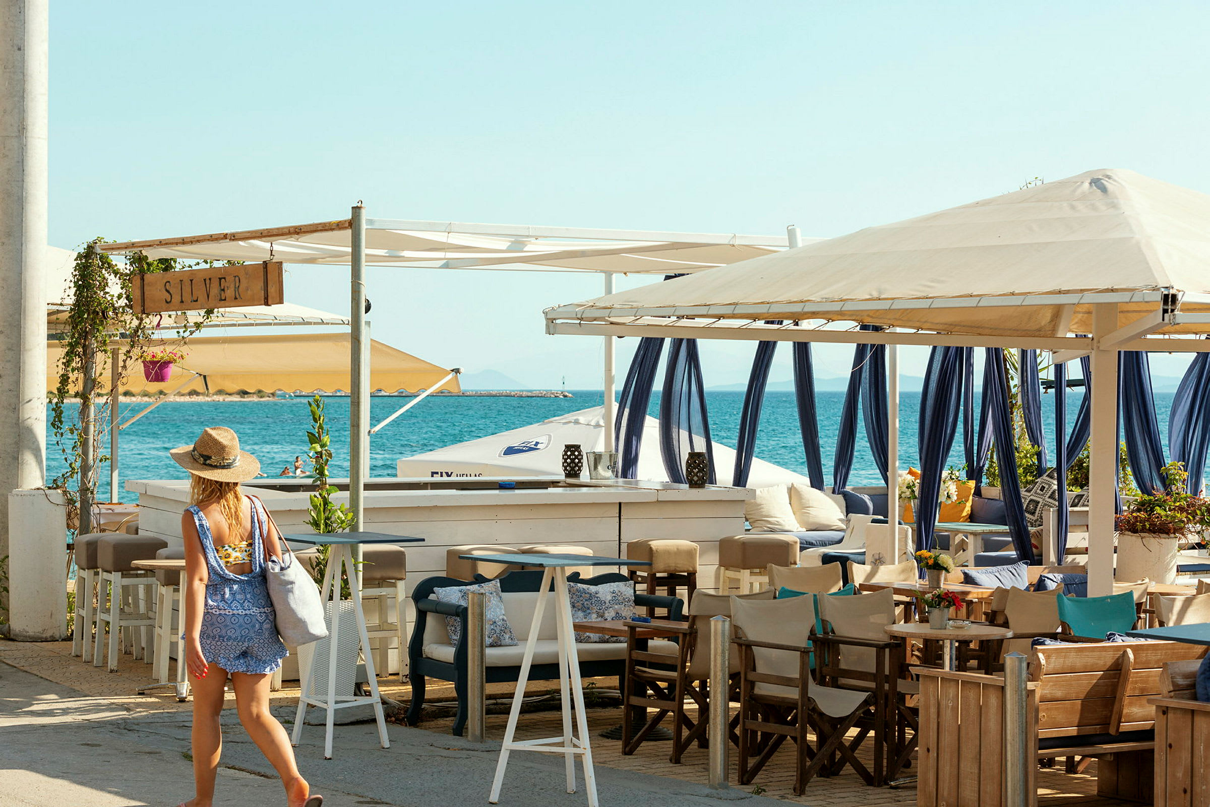 Billede af en person, der går ved en strandbar med siddepladser og havet i baggrunden. (AI-genereret tekst)