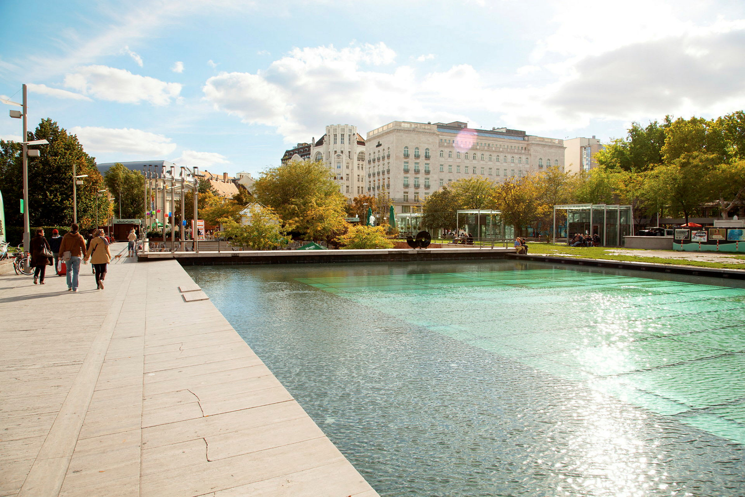 En gangsti ved en moderne park med en reflekterende vandflade og grønne omgivelser. (AI-genereret tekst)