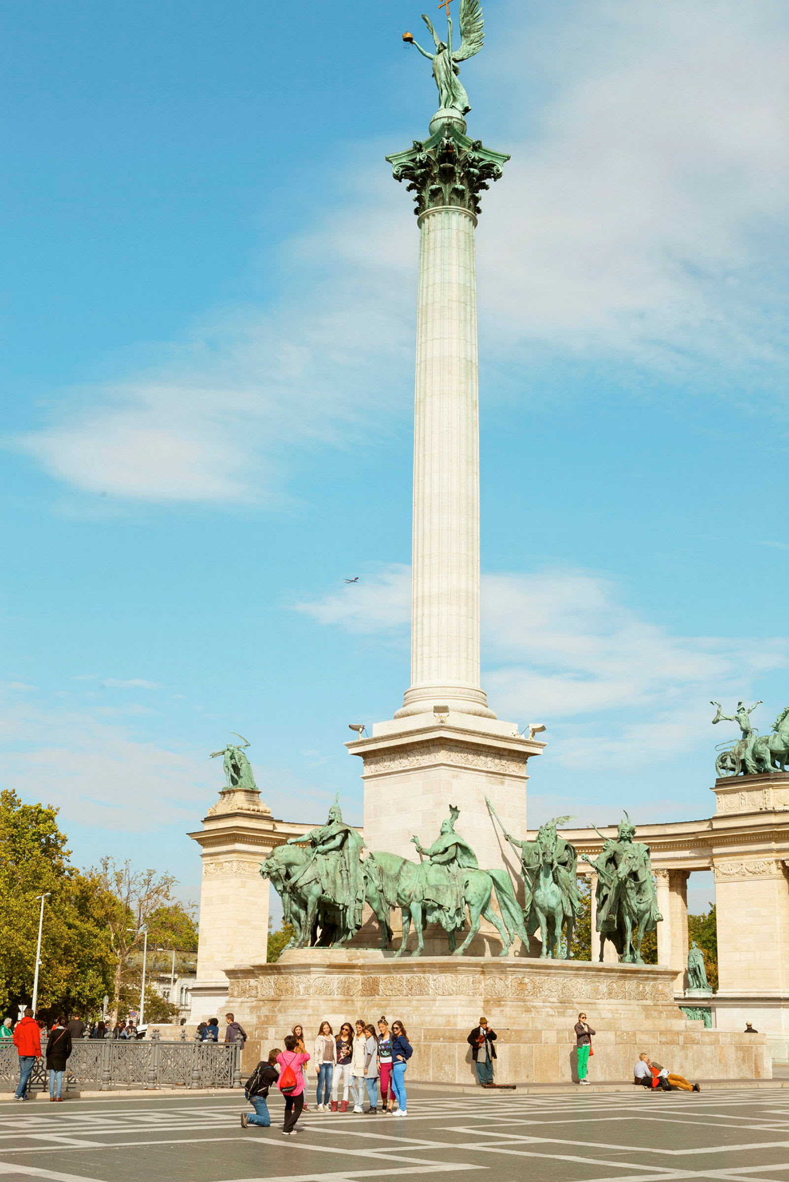 En høj søjle med en statue på toppen, omgivet af flere rytterskulpturer ved et monument på en åben plads. (AI-genereret tekst)