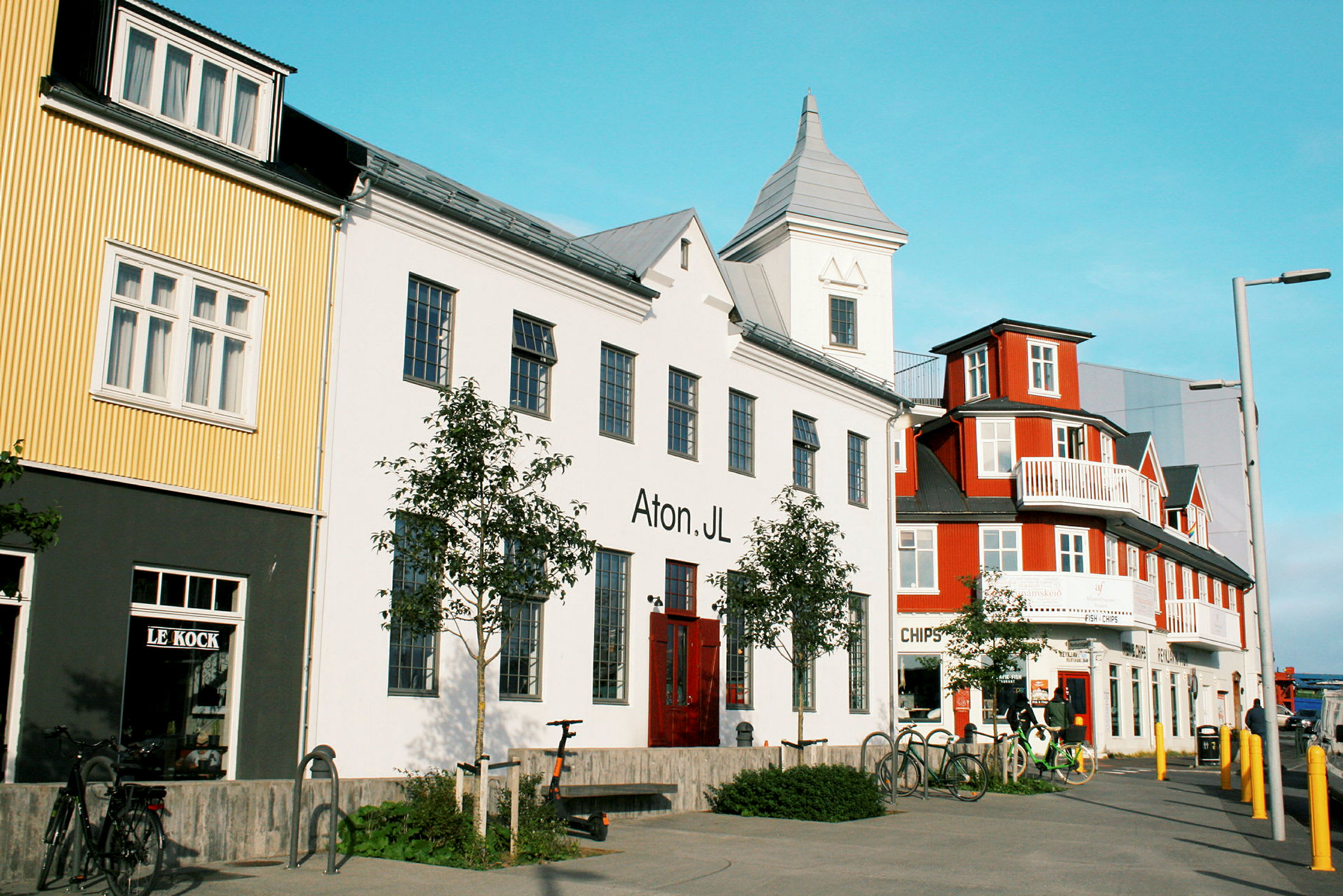 Flere farverige bygninger langs en gade med cykler parkeret foran. (AI-genereret tekst)