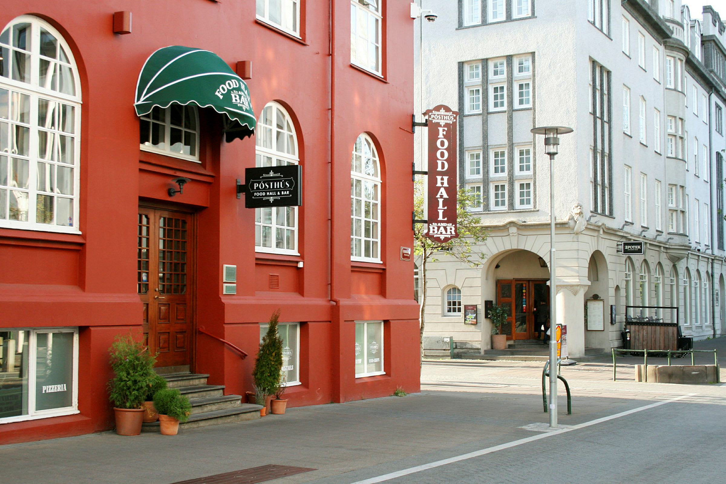 Et rødt hus med store vinduer og en grøn markise, hvor der står "Food Hall & Bar". (AI-genereret tekst)