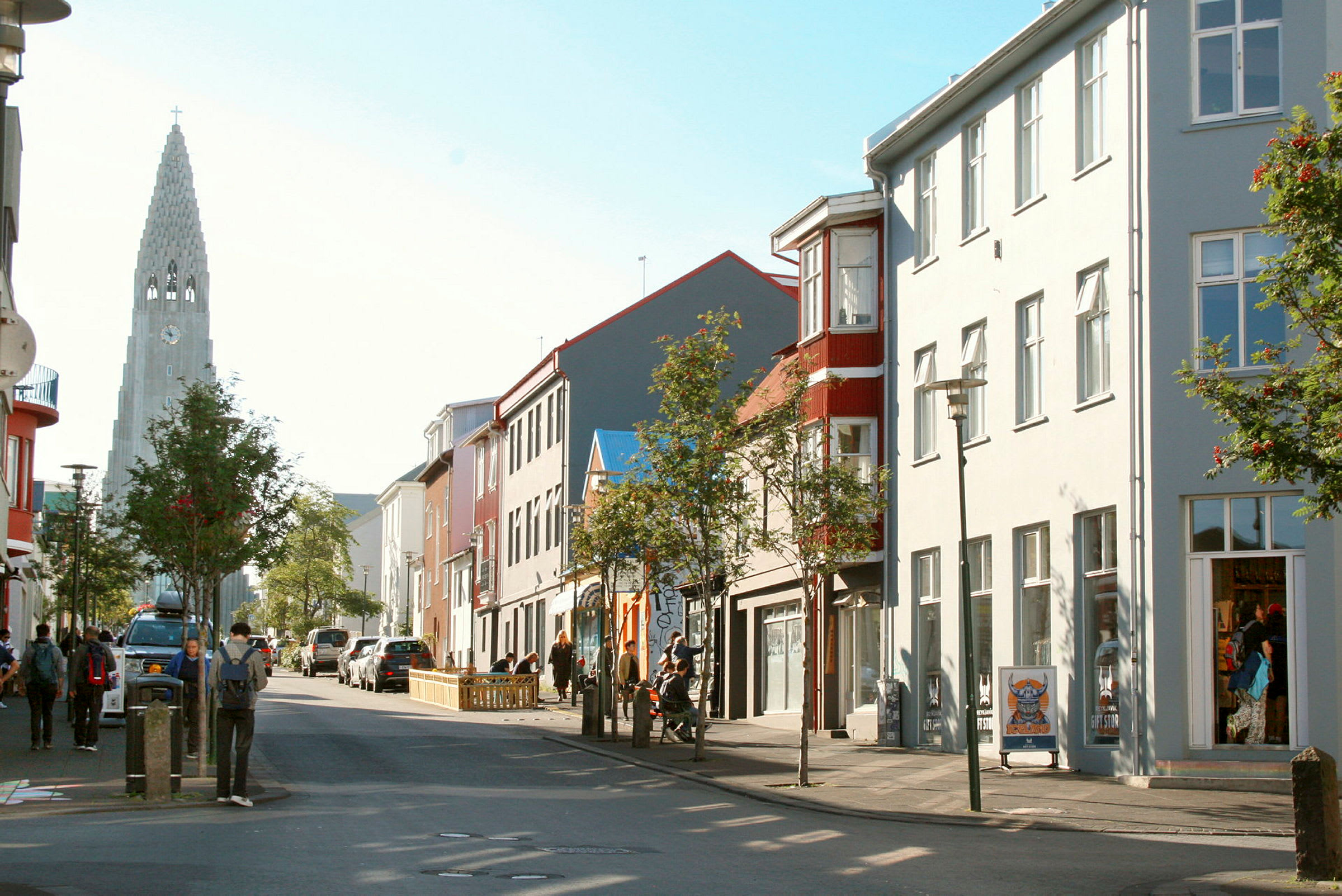 En gade med mennesker, bygninger og en kirke med spir i baggrunden. (AI-genereret tekst)