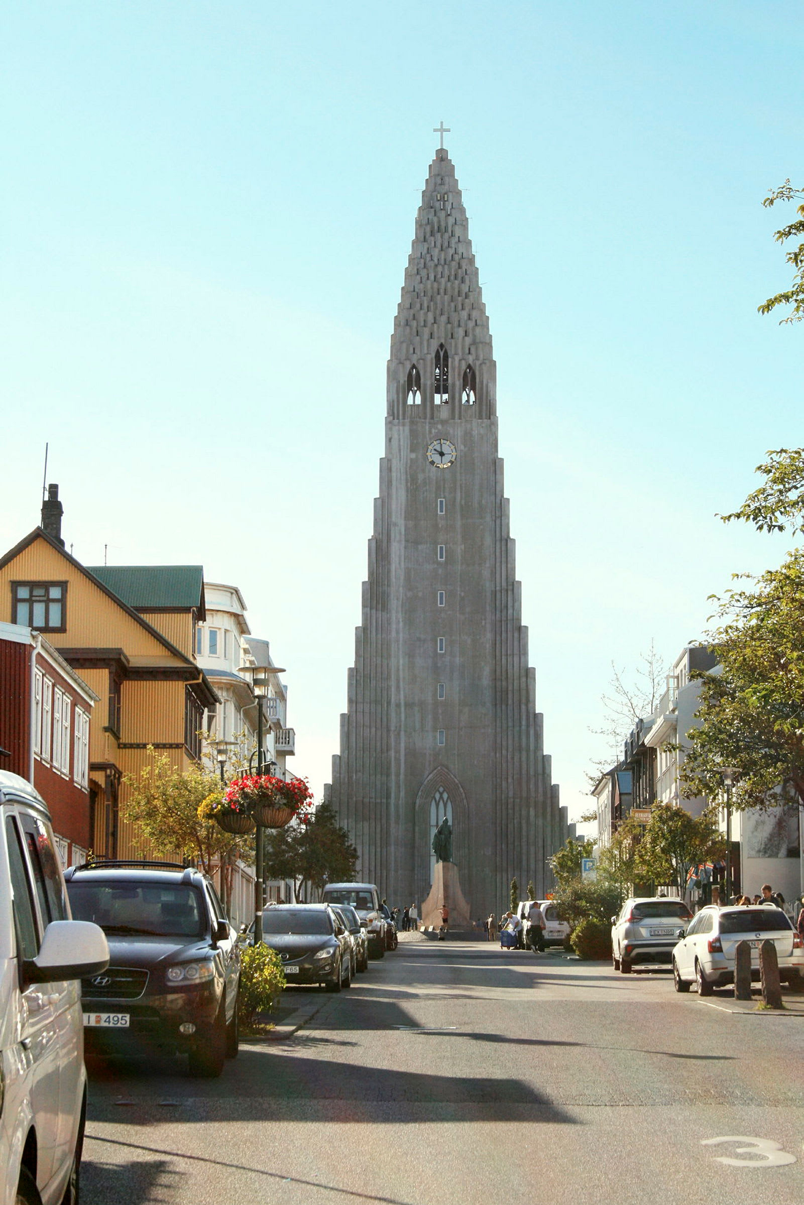 Et billede af en gade med biler parkeret langs siderne, og i baggrunden ses en høj kirke med unik arkitektur. (AI-genereret tekst)
