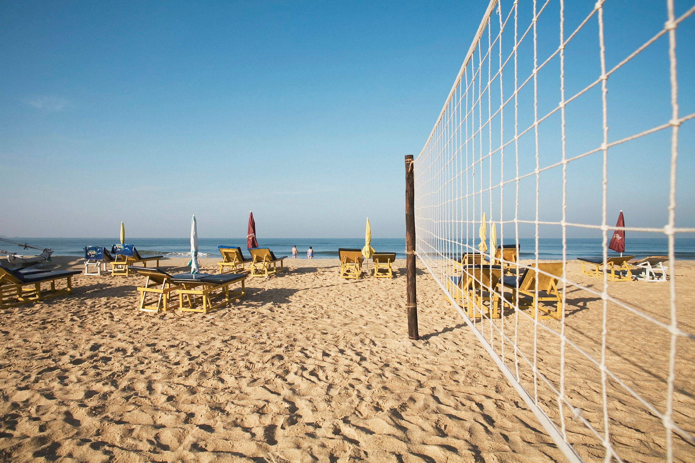 Strand med liggestole, parasoller og et volleyballnet. (AI-genereret tekst)