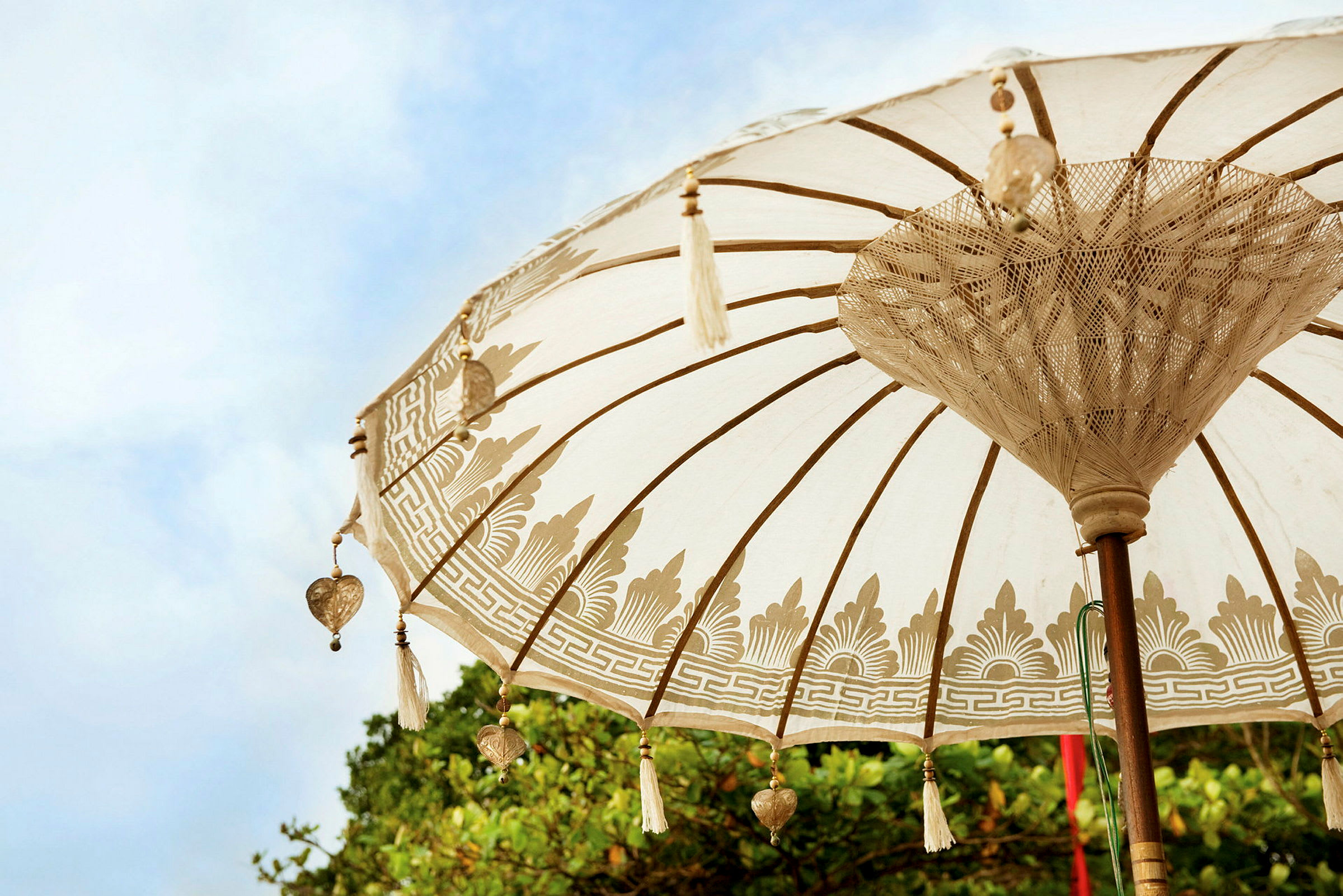En dekoreret parasol med mønstre og hængende pynt, mod en baggrund af blå himmel og grønt. (AI-genereret tekst)