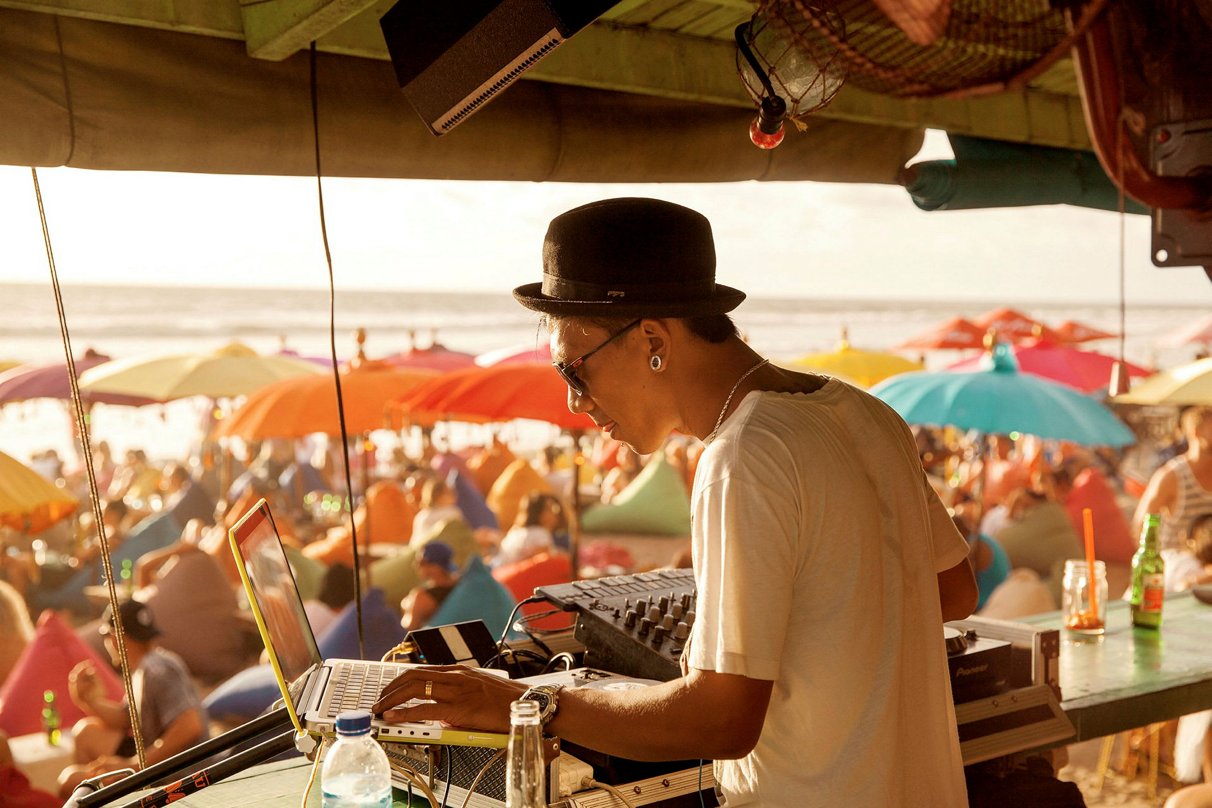 Person arbejder ved DJ-udstyr nær stranden med paraplyer i baggrunden. (AI-genereret tekst)
