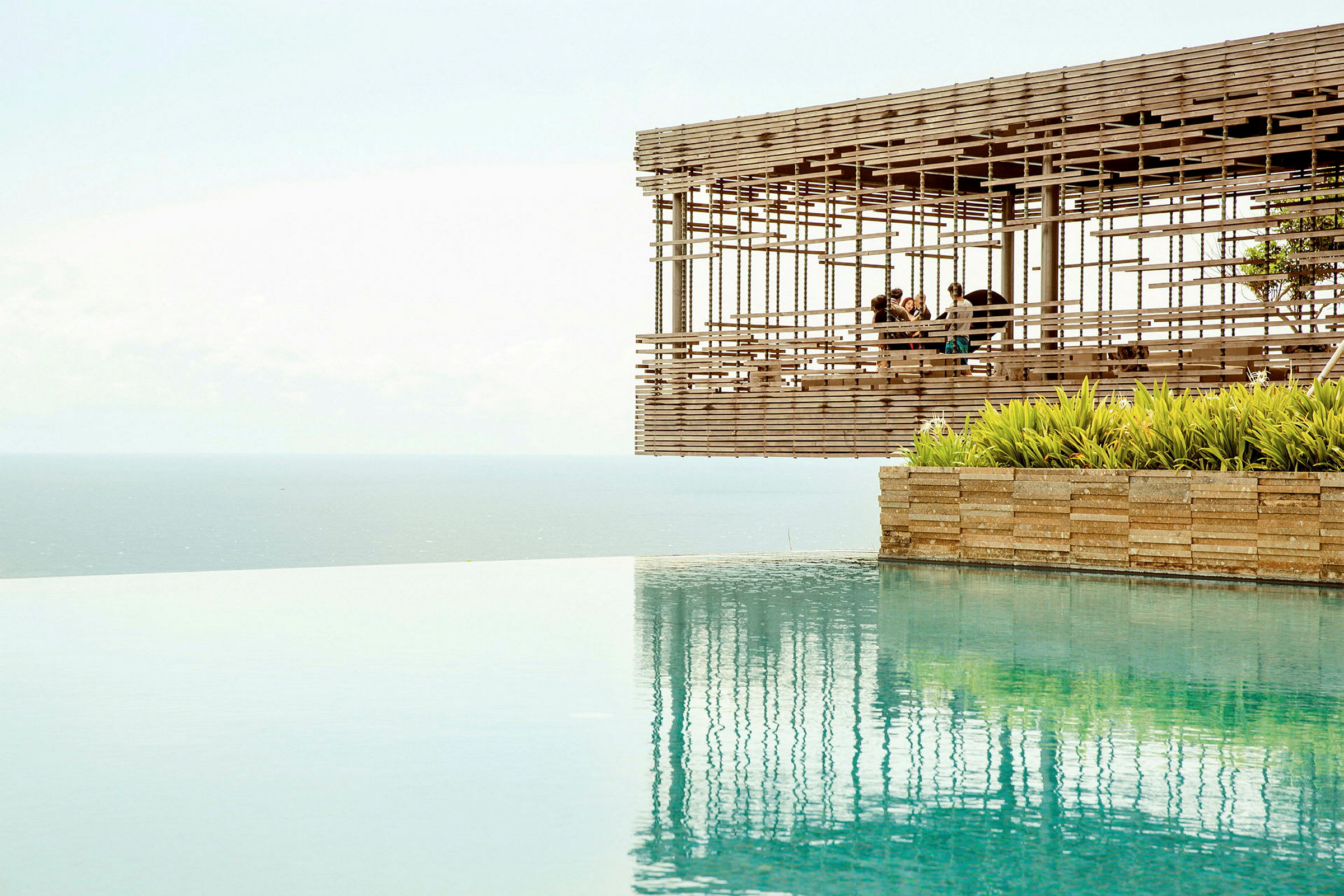 Udsigt over en infinitypool med havet i baggrunden og en træpavillon, der svæver ved kanten. (AI-genereret tekst)