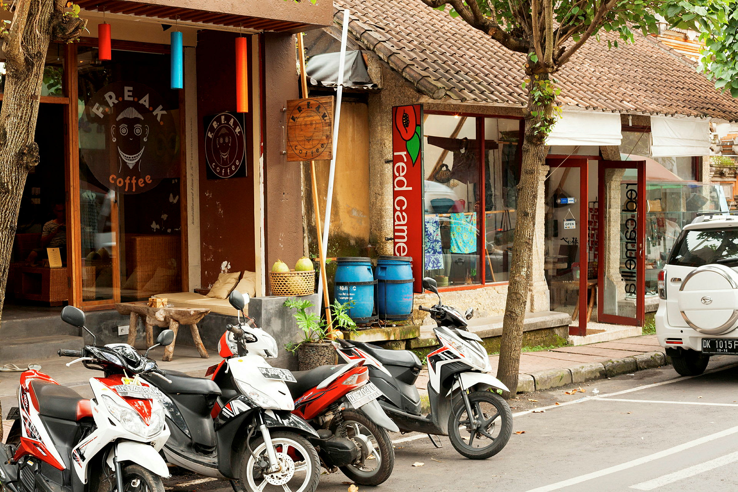 En gade med parkerede motorcykler foran en café og butikker. (AI-genereret tekst)