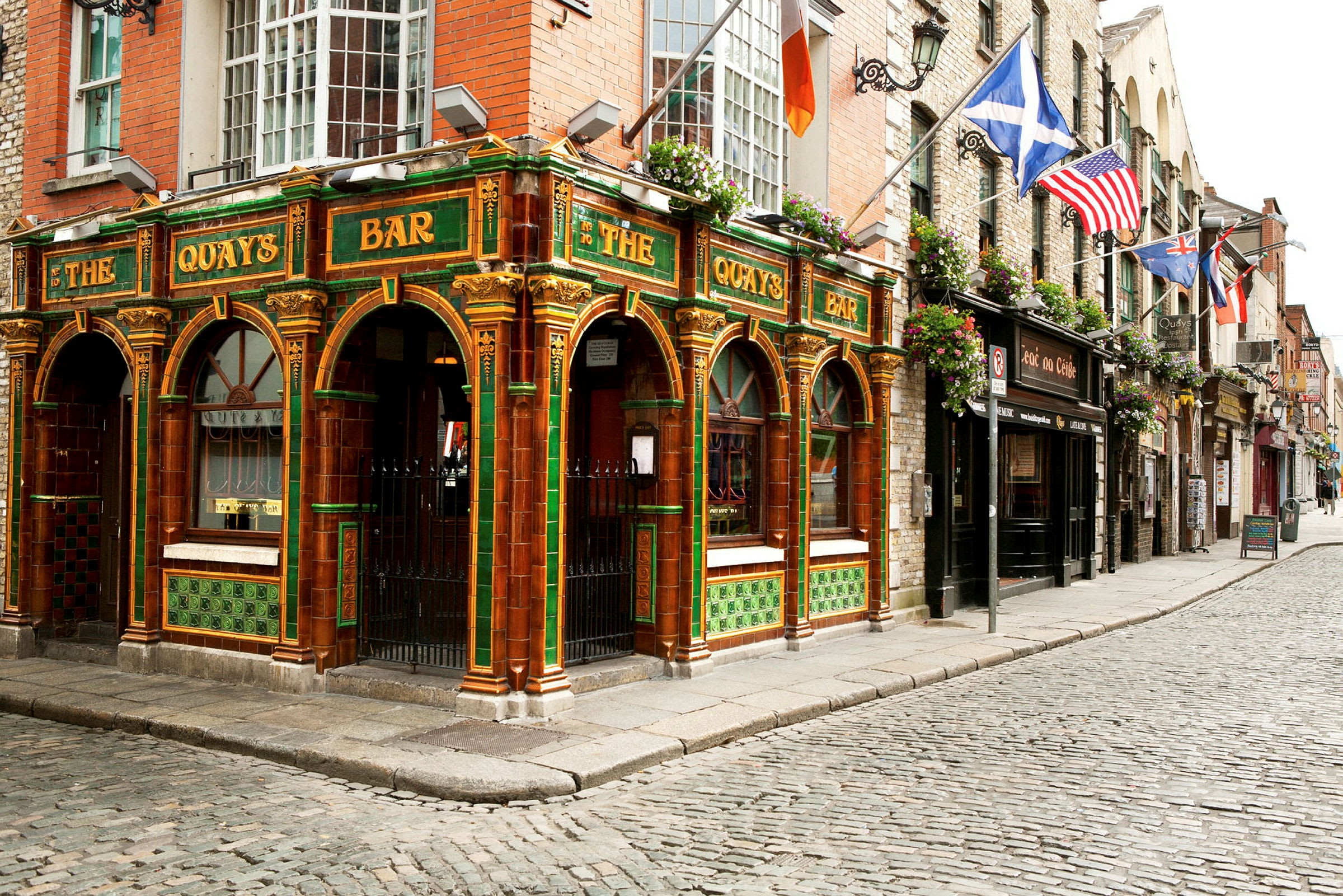 En farverig pub med grøn og orange dekoration i traditionel stil ligger ved en brostensbelagt gade. (AI-genereret tekst)