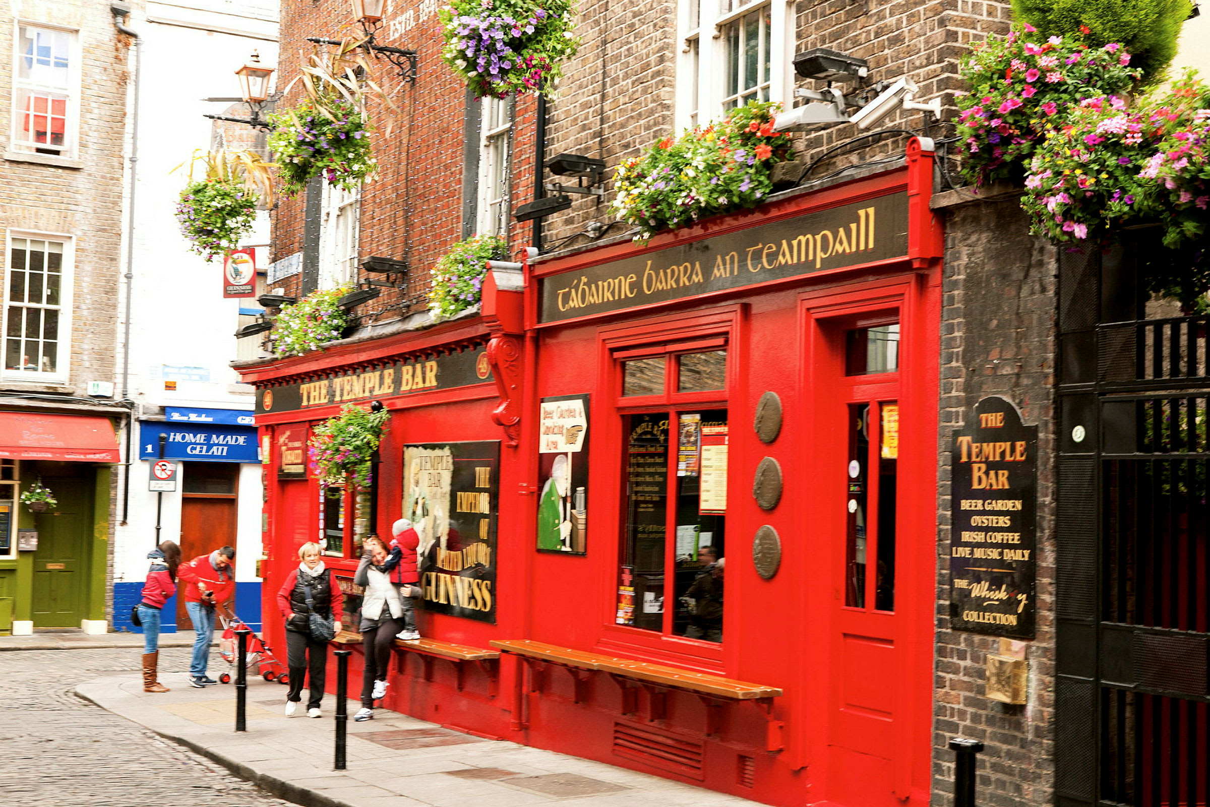 En rød bygning med skiltet 'The Temple Bar' med blomsterkasser og folk udenfor. (AI-genereret tekst)