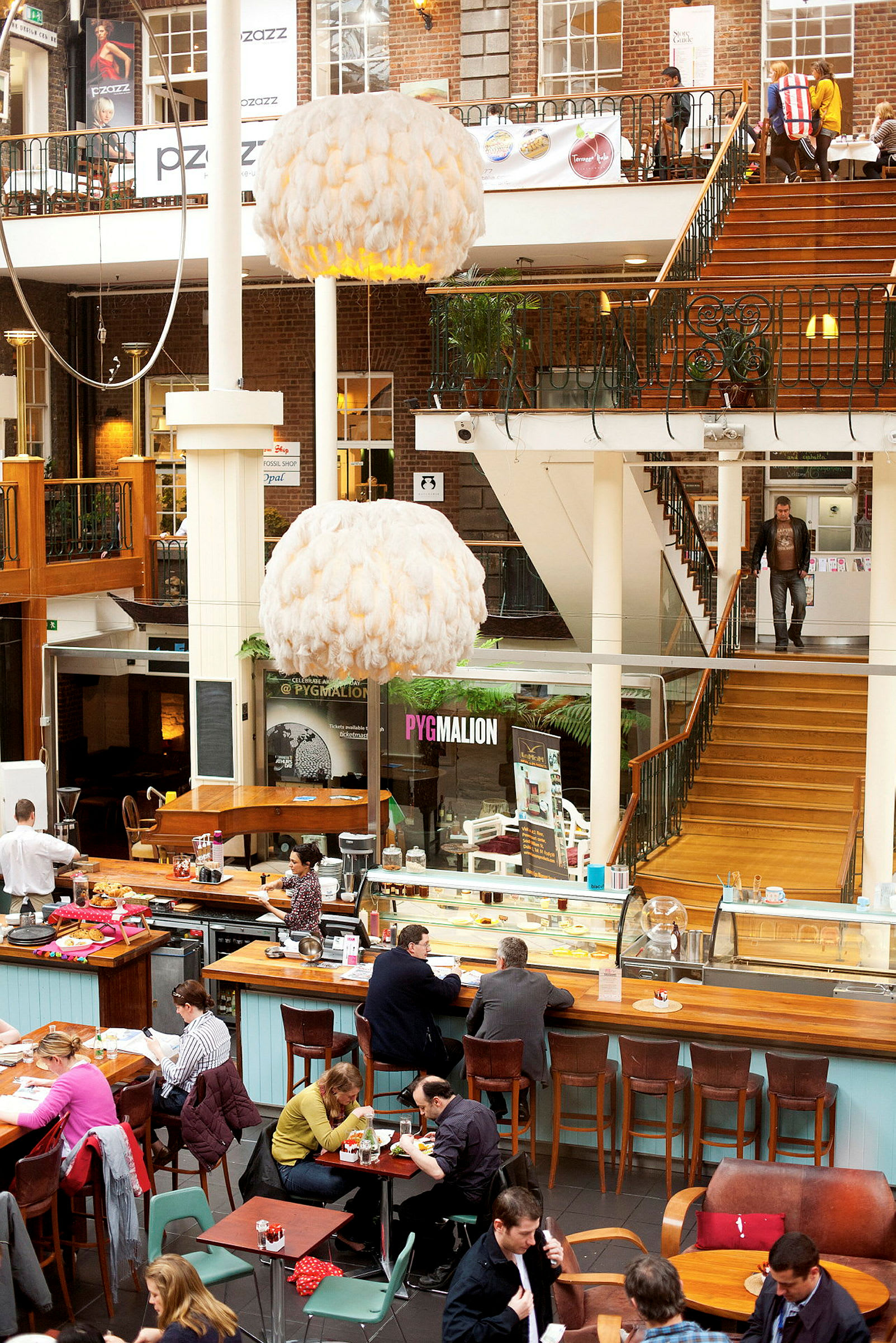 En indendørs restaurant med siddepladser og en bar i stueetagen og en overetage med gelænder. (AI-genereret tekst)