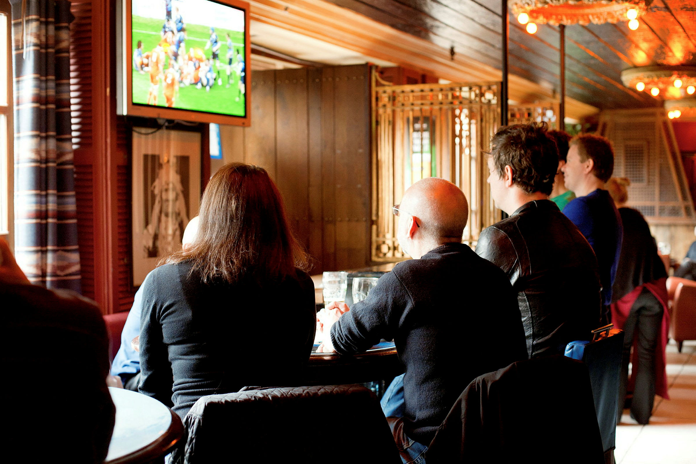 Personer sidder i en lokal og ser på sport på en TV-skærm. (AI-genereret tekst)